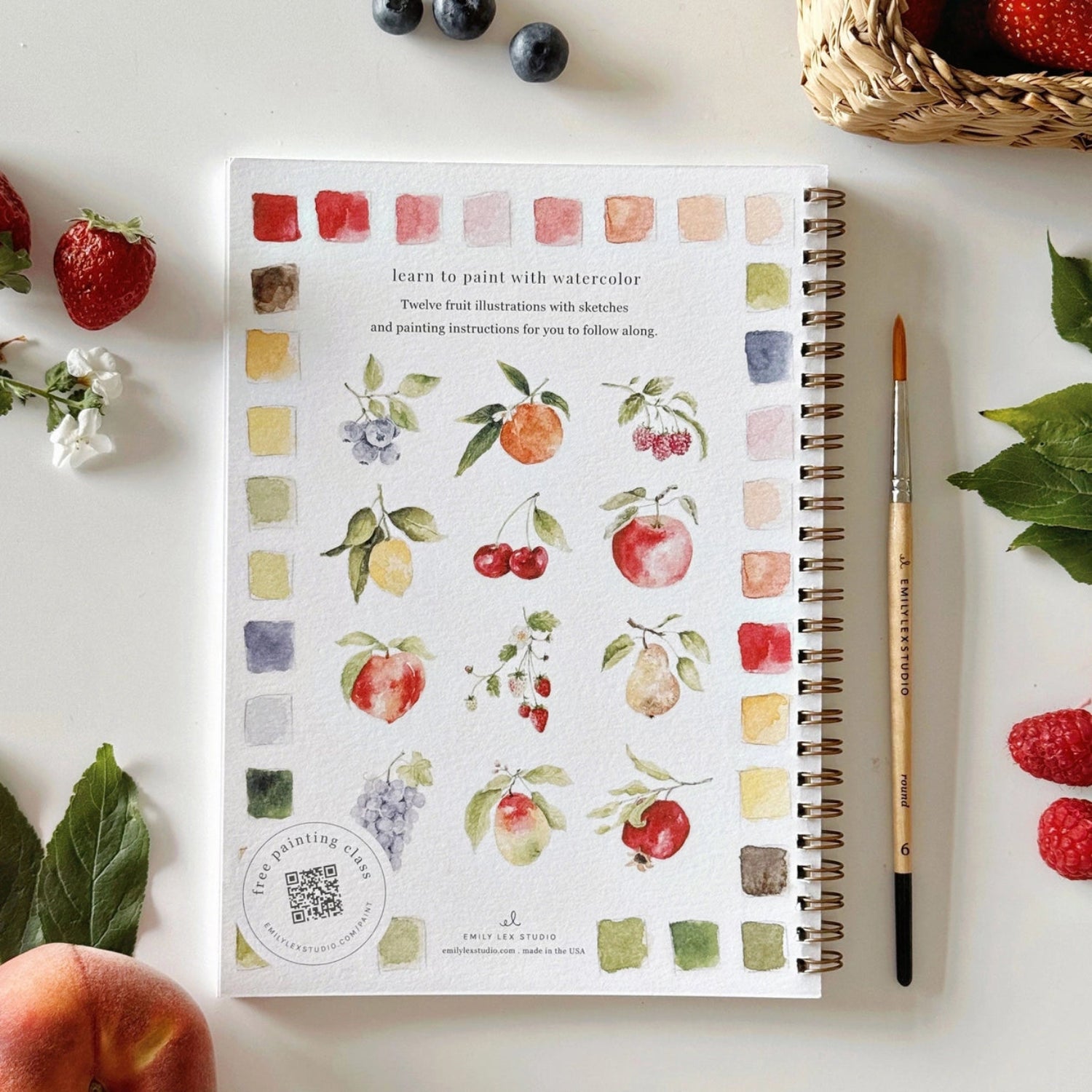 Notebook with fruit illustrations on a table with fruits and a brush