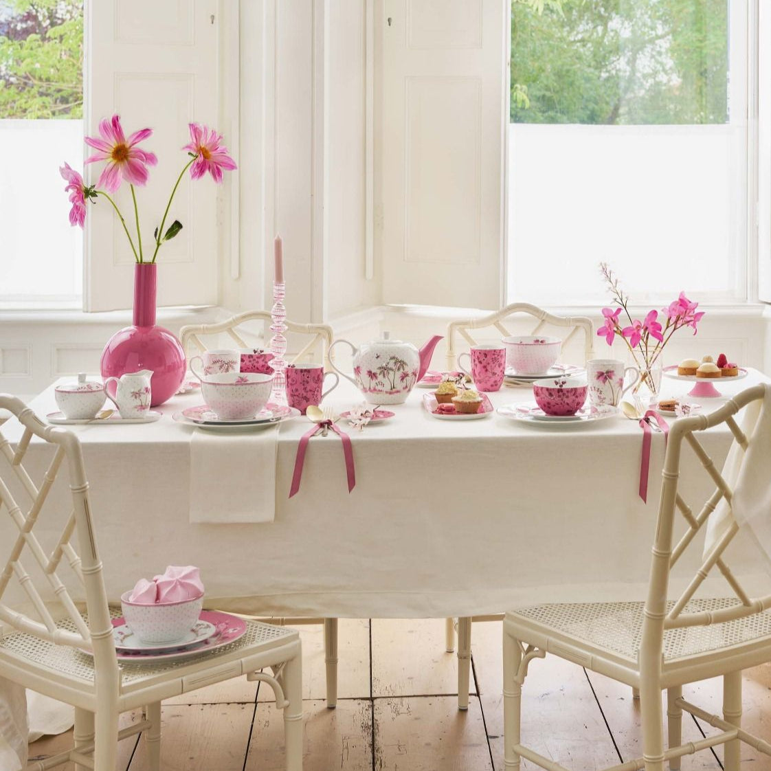 Dining room with a table set for a meal, featuring pink flowers and decor.