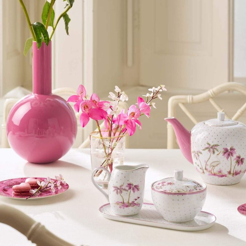 Tea set with floral design on a table with pink and white flowers.