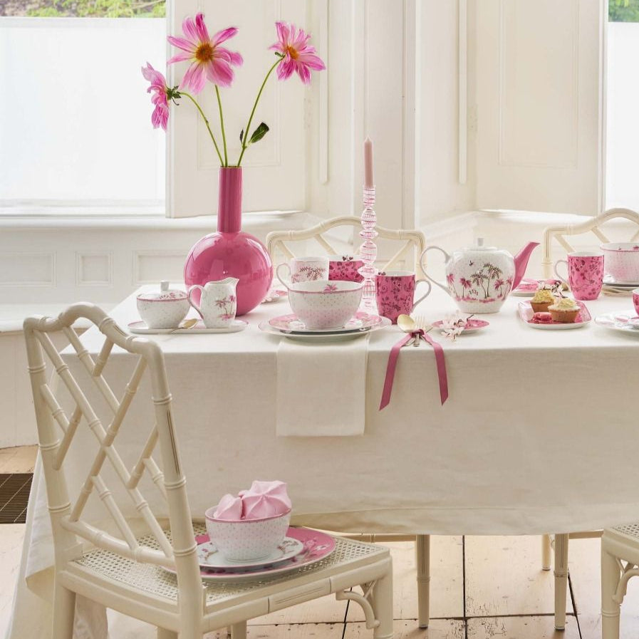 Dining room with a table set for a meal, featuring pink flowers and decor.