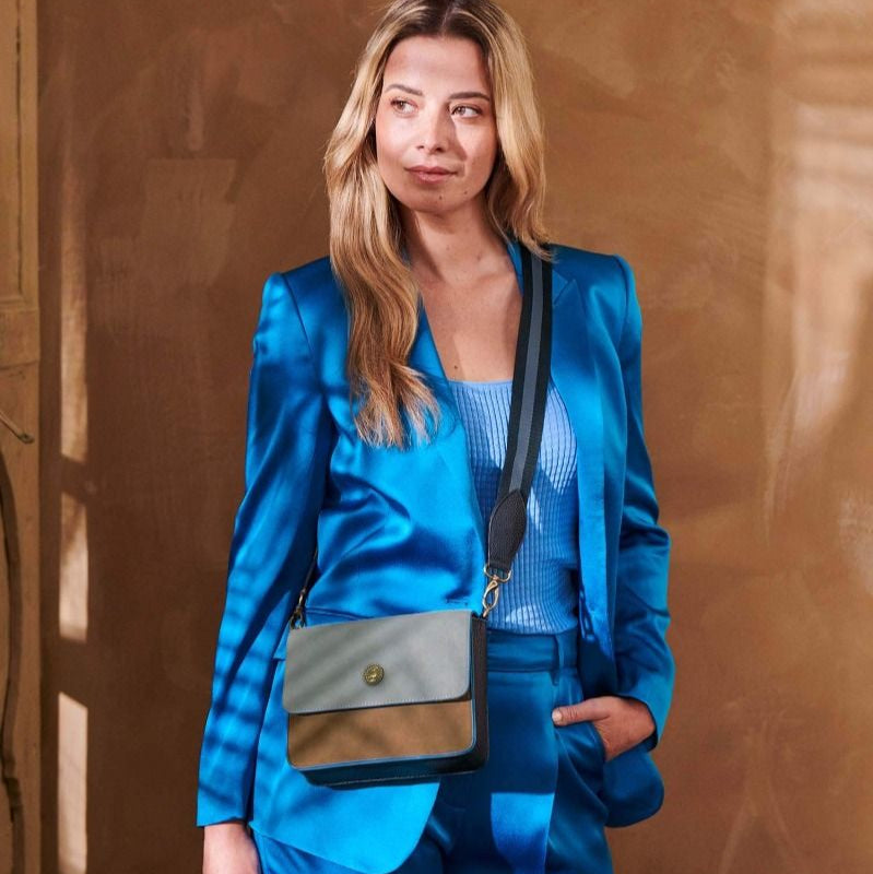 Woman in a blue suit holding a crossbody bag against a brown wall
