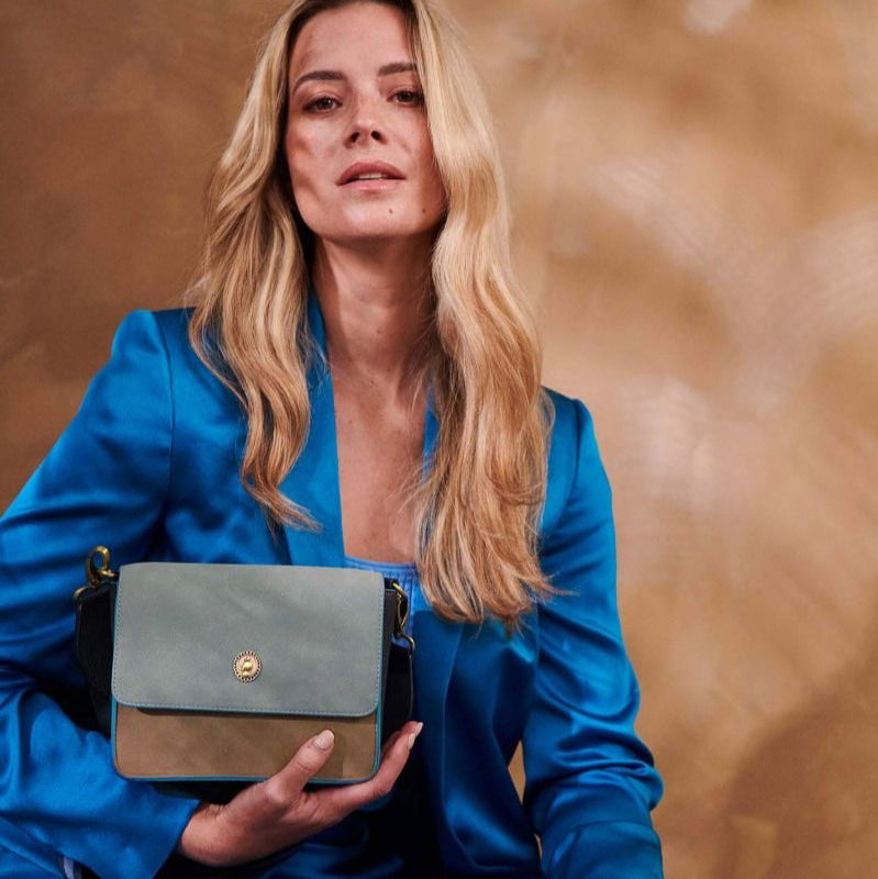 Woman in a blue outfit holding a blue handbag against a brown background