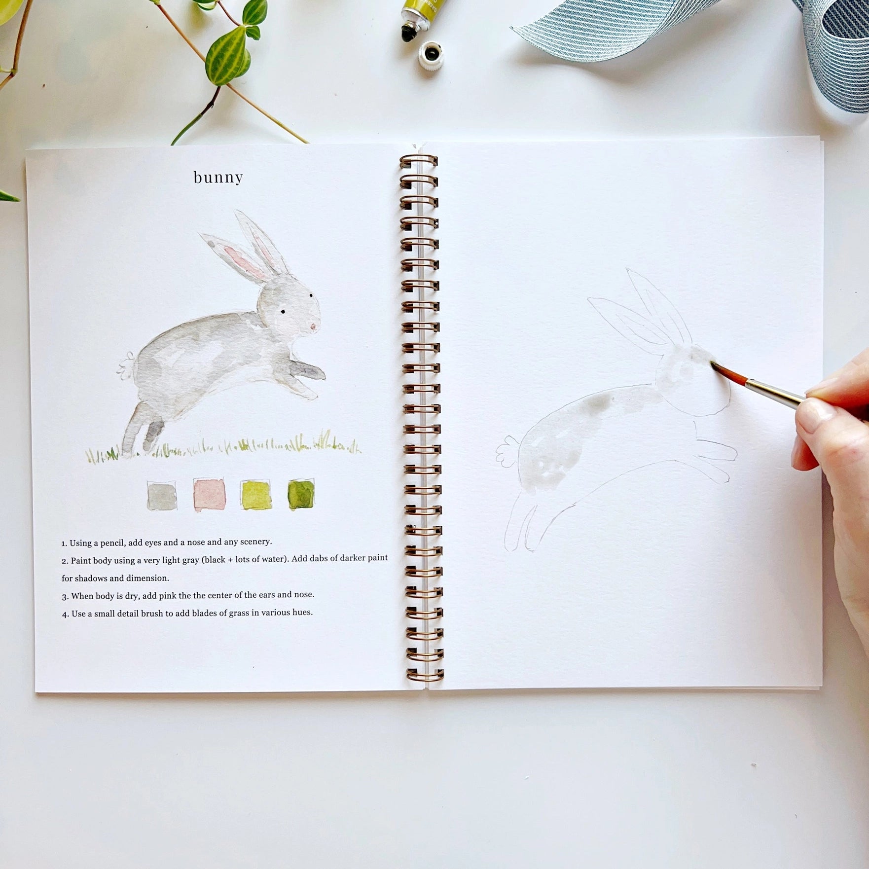 Open book with a rabbit illustration and painting activity, held by a hand with a paintbrush.