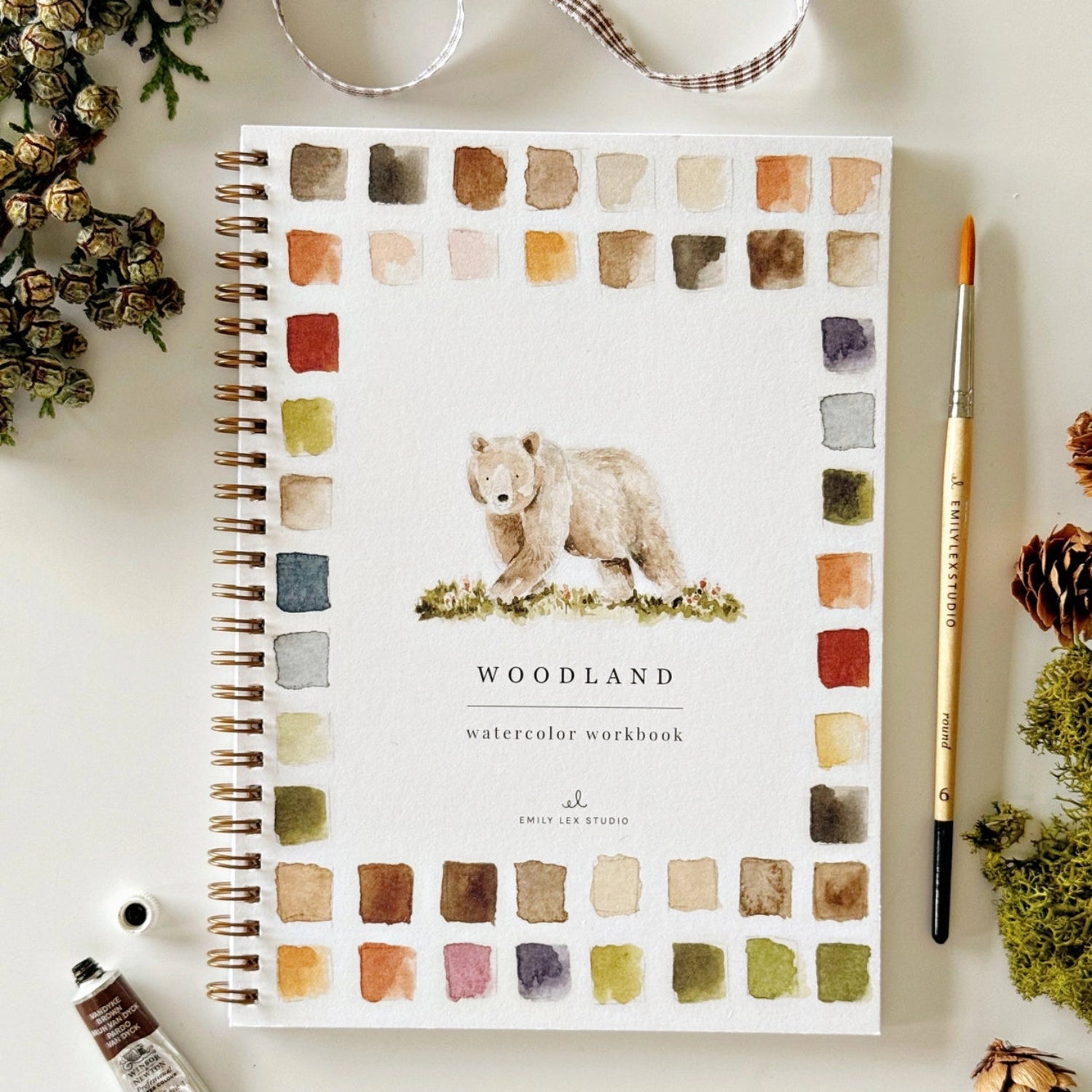 Notebook with bear illustration and watercolor swatches on a white surface with decorative items.