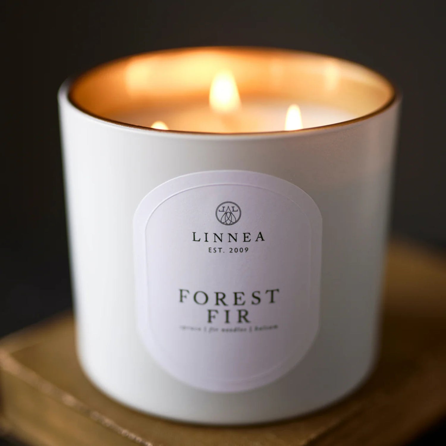 Lit candle in a white container with 'LINNEA' label on a dark background