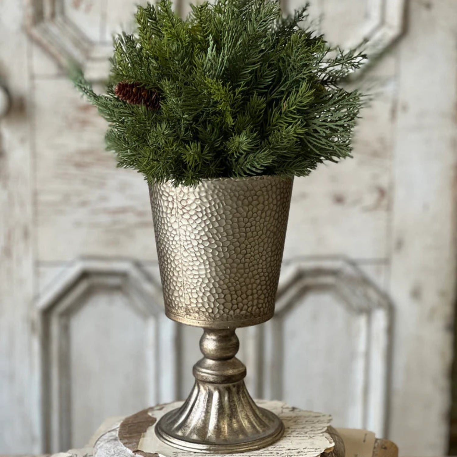 Decorative vase with greenery on a wooden surface against a textured wall.