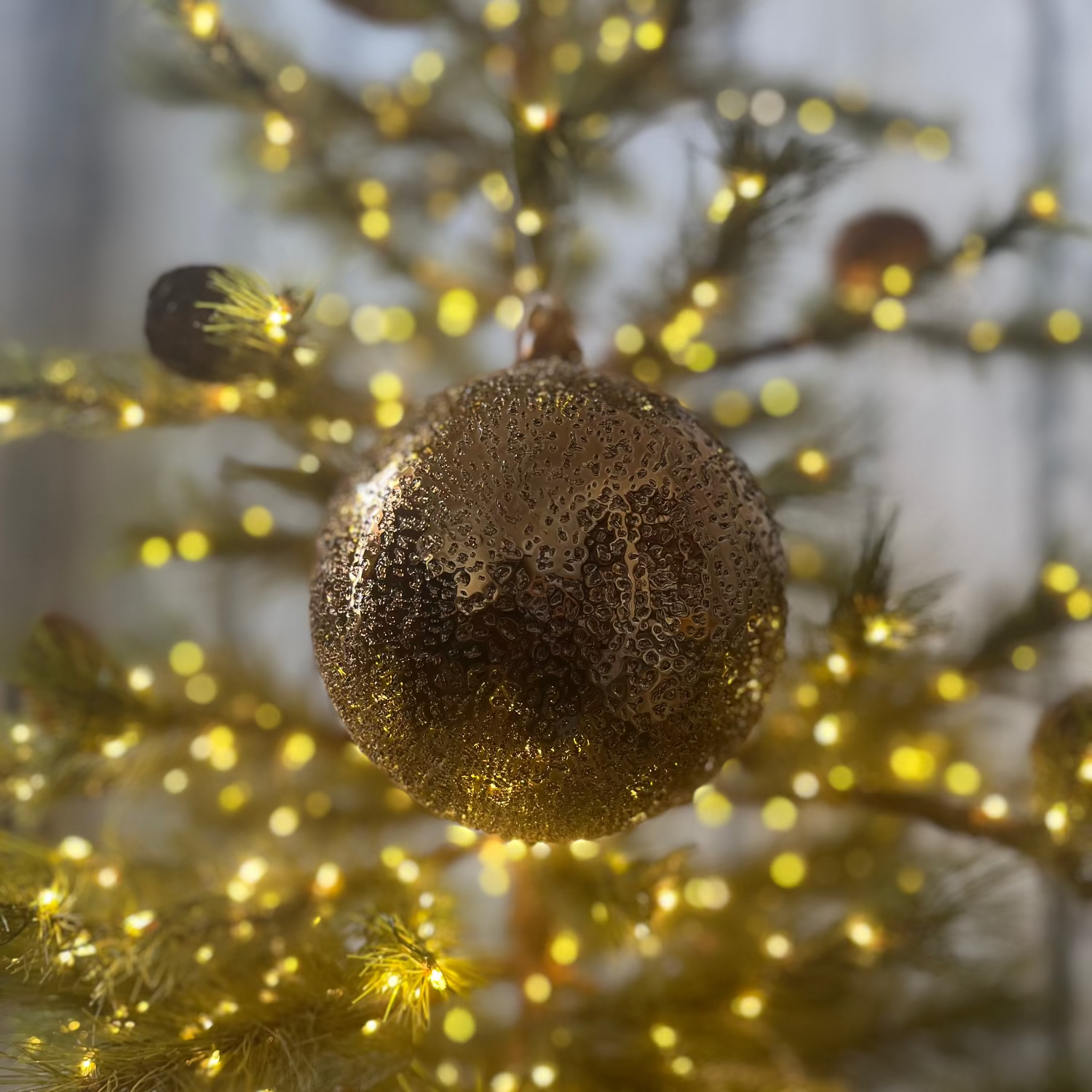 Gold glittery ornament on a tree with blurred lights in the background