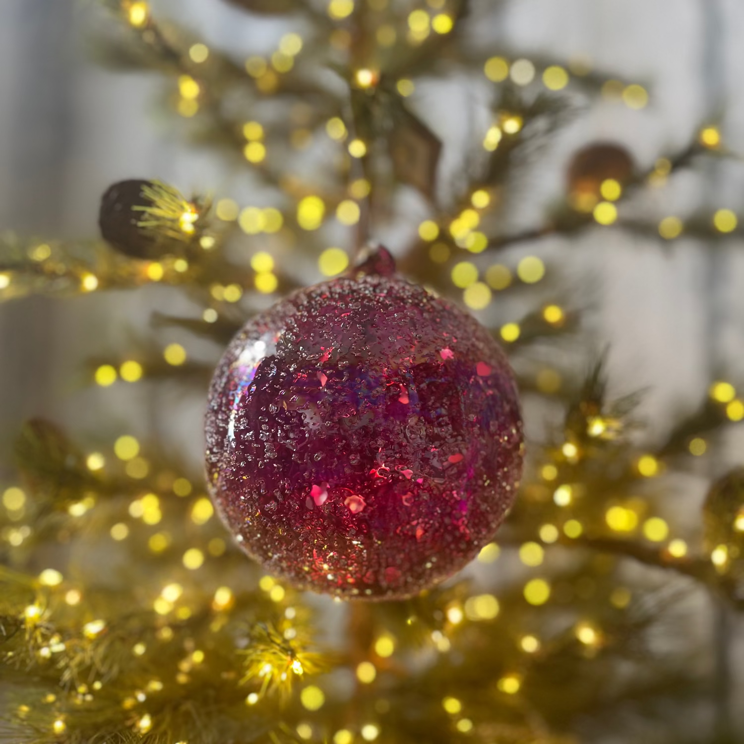 Pink glittery ornament on a Christmas tree with blurred lights in the background