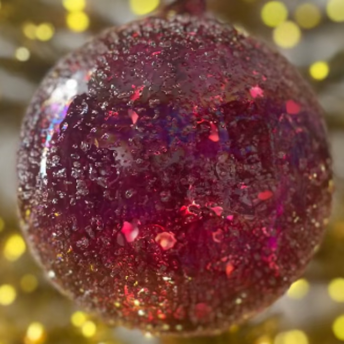 Pink glittery ornament on a Christmas tree with blurred lights in the background