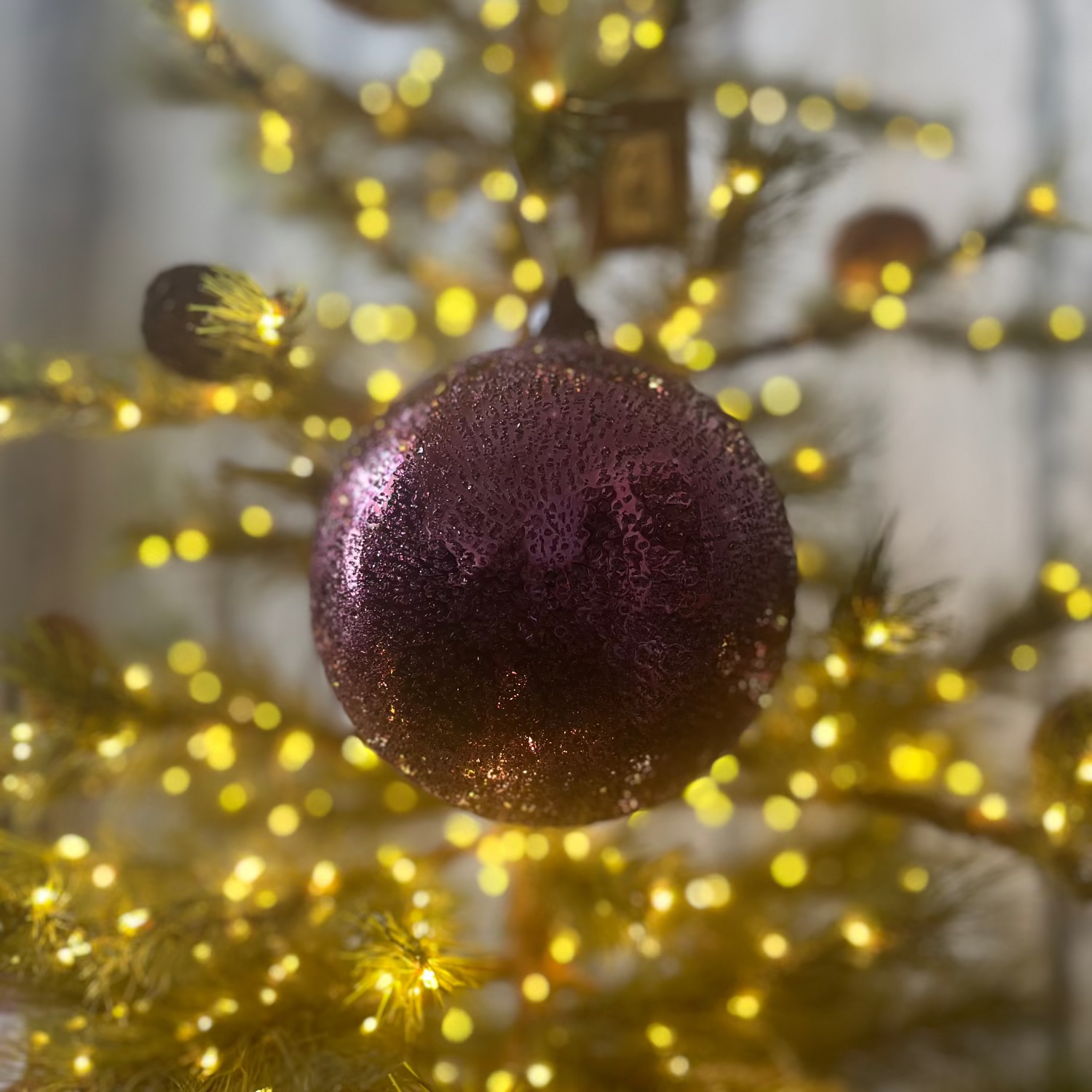 Purple glittery ornament on a Christmas tree with blurred lights in the background