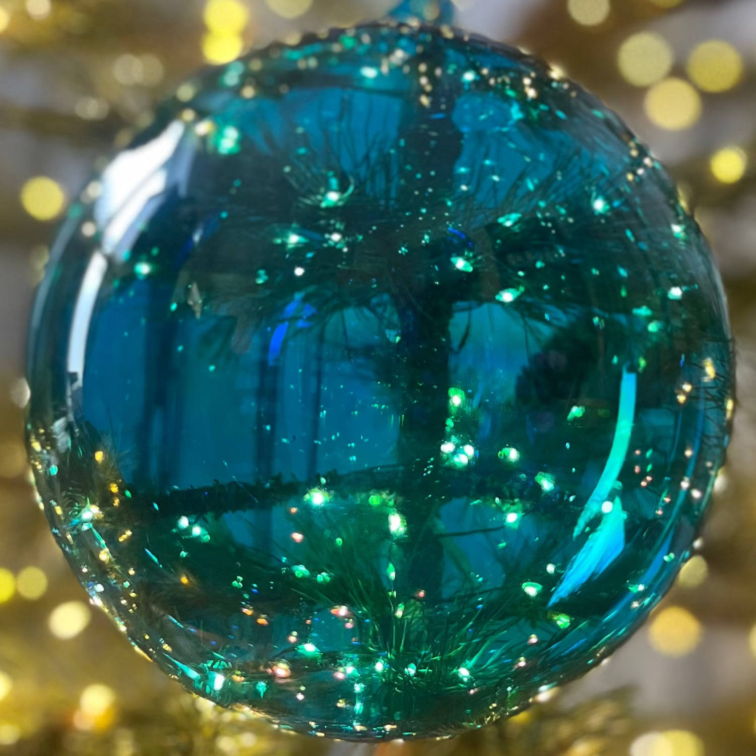 Blue glittery Christmas ornament on a tree with blurred lights in the background