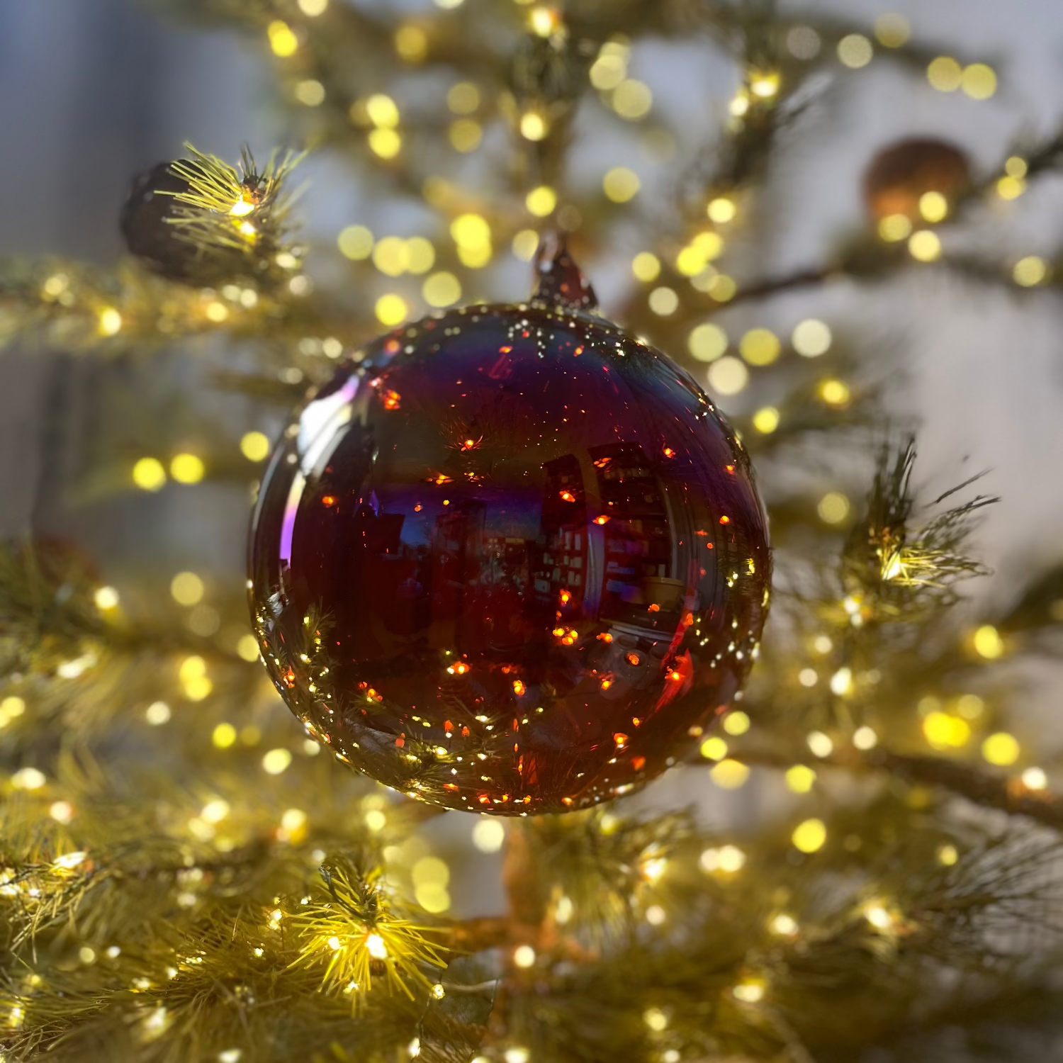 Decorative red ornament on a Christmas tree with blurred lights in the background