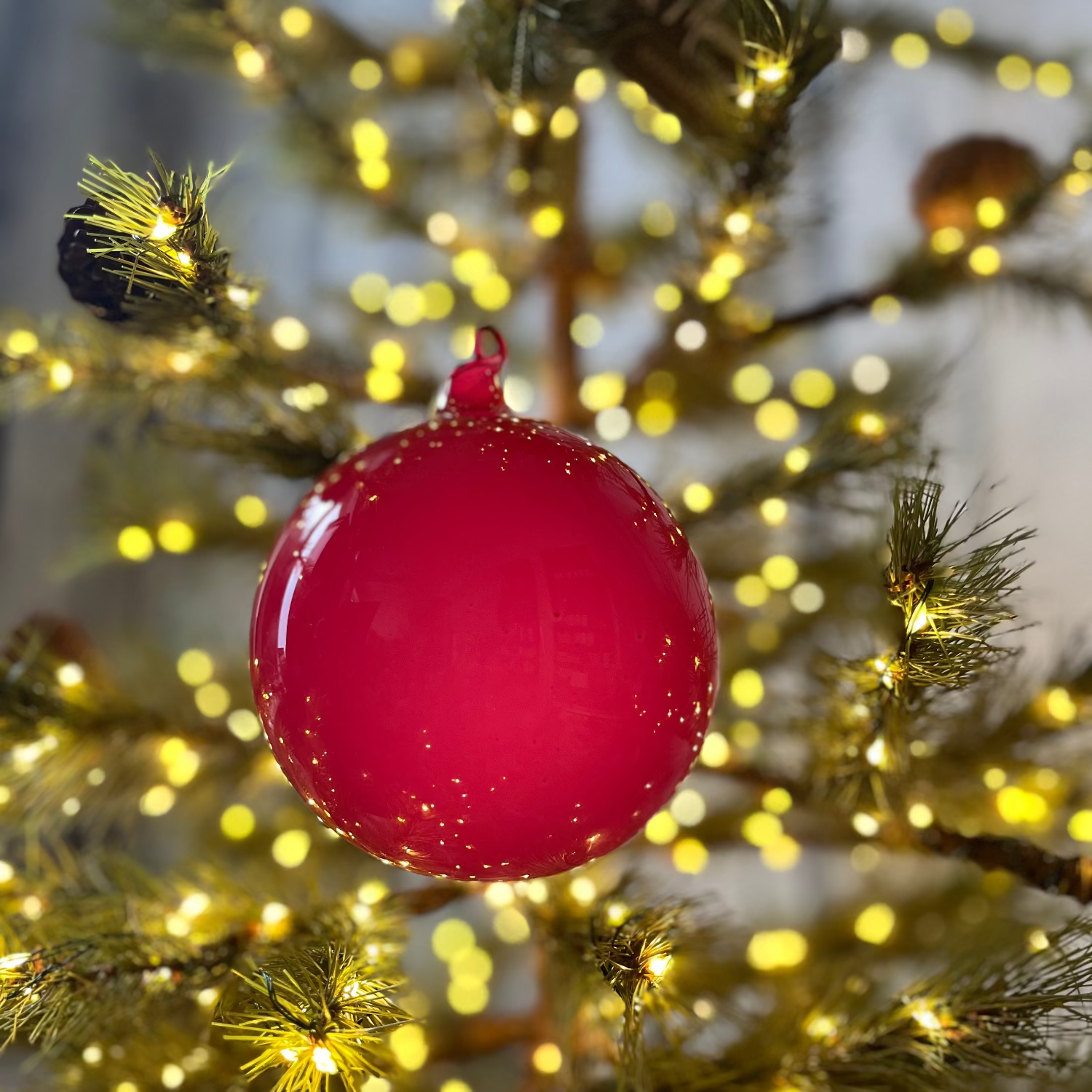 Red Christmas ornament on a tree with blurred lights in the background