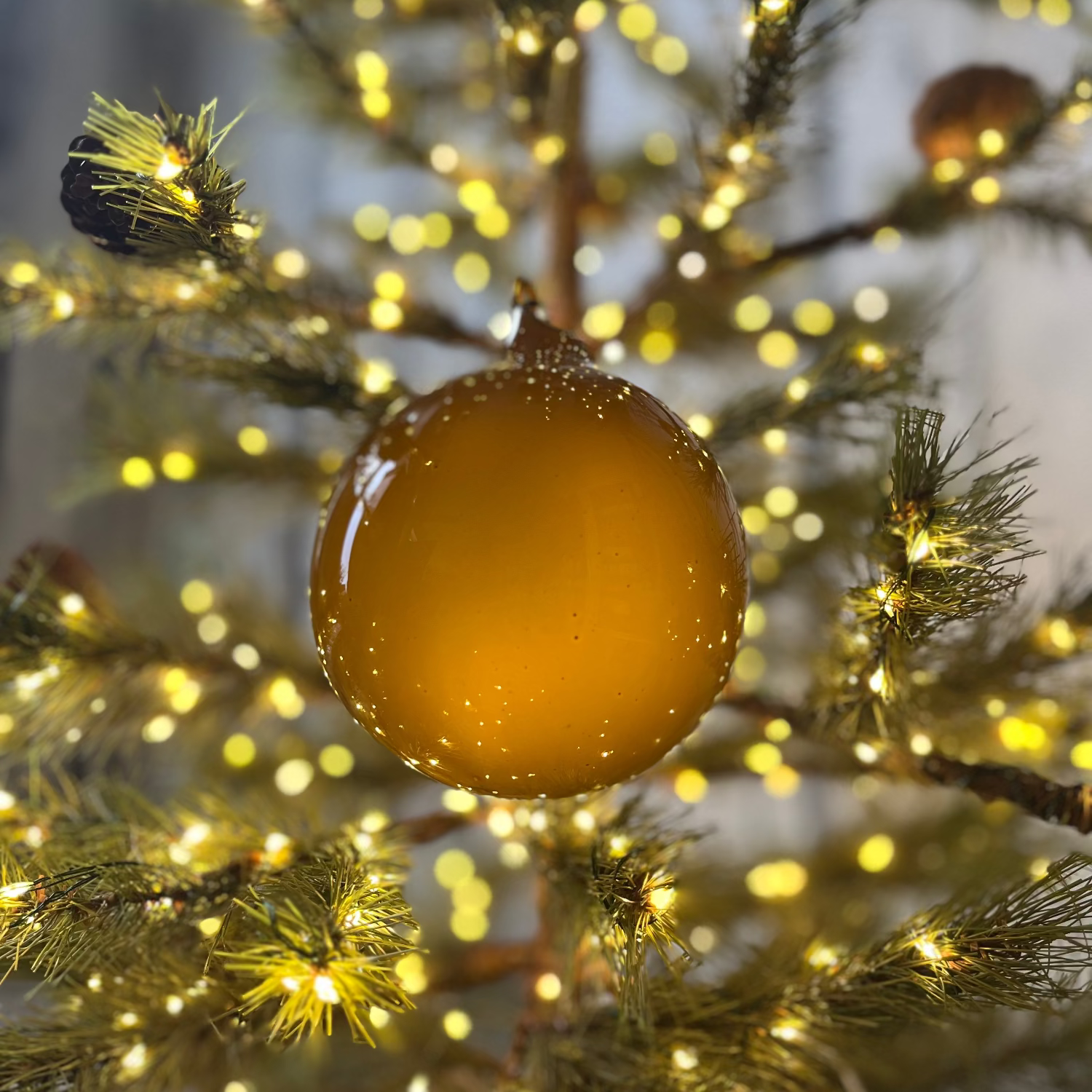 Gold Christmas ornament on a tree with blurred lights in the background