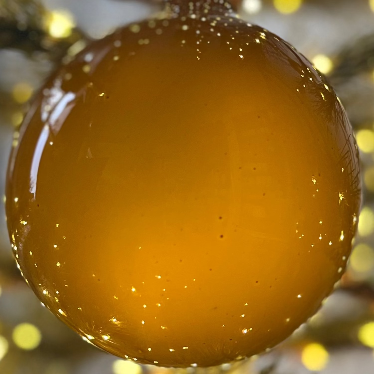 Gold Christmas ornament on a tree with blurred lights in the background