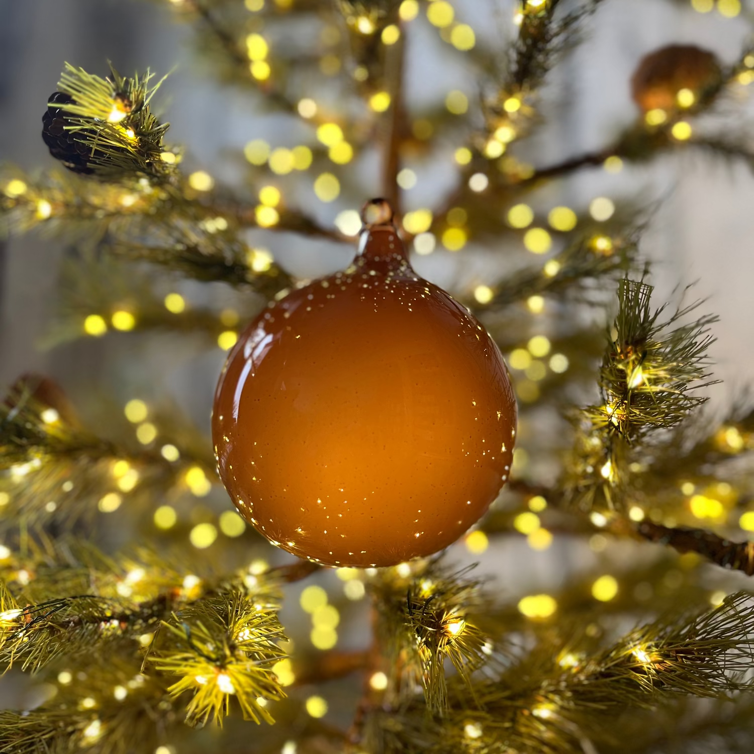 Decorative brown ornament on a lit Christmas tree with blurred lights in the background