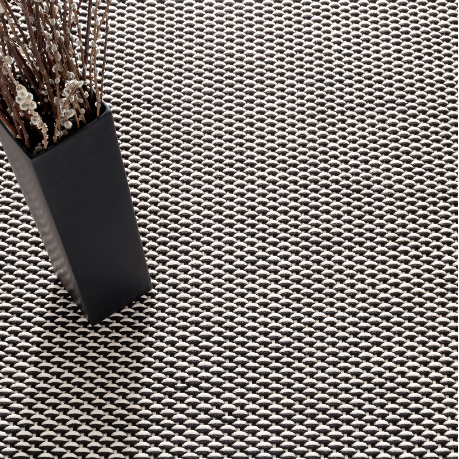 Textured woven surface with a black pot and dried plants on a white background
