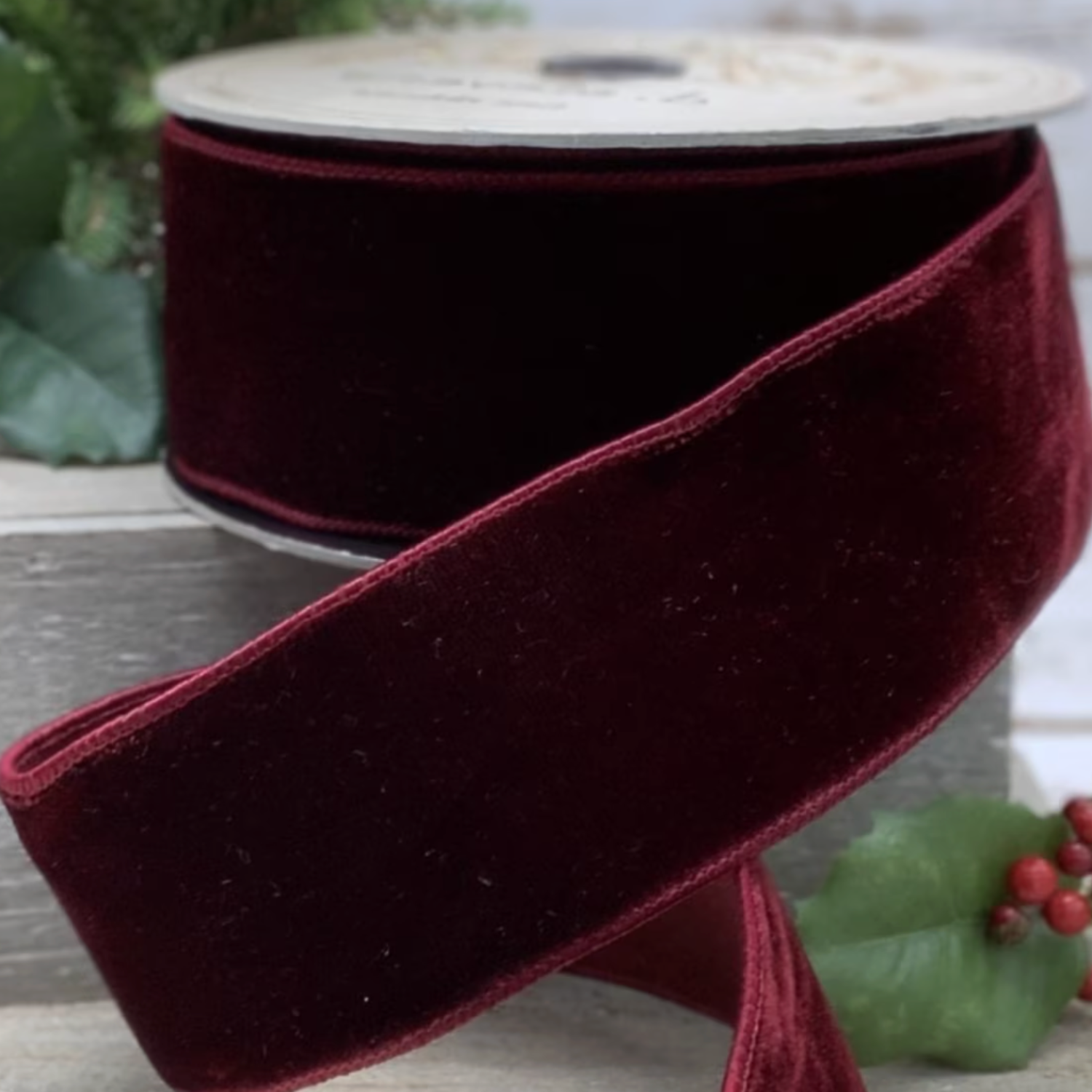 Burgundy velvet ribbon with a white label on a wooden surface with greenery in the background