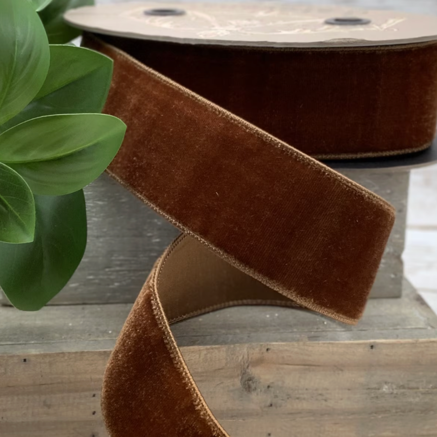 Brown velvet ribbon on a wooden spool with a plant in the background
