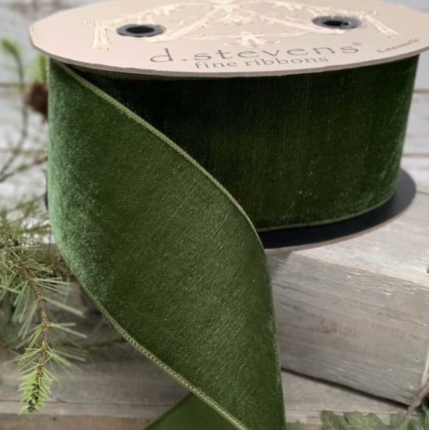 Spool of green ribbon with a visible brand label on a wooden surface with leaves.