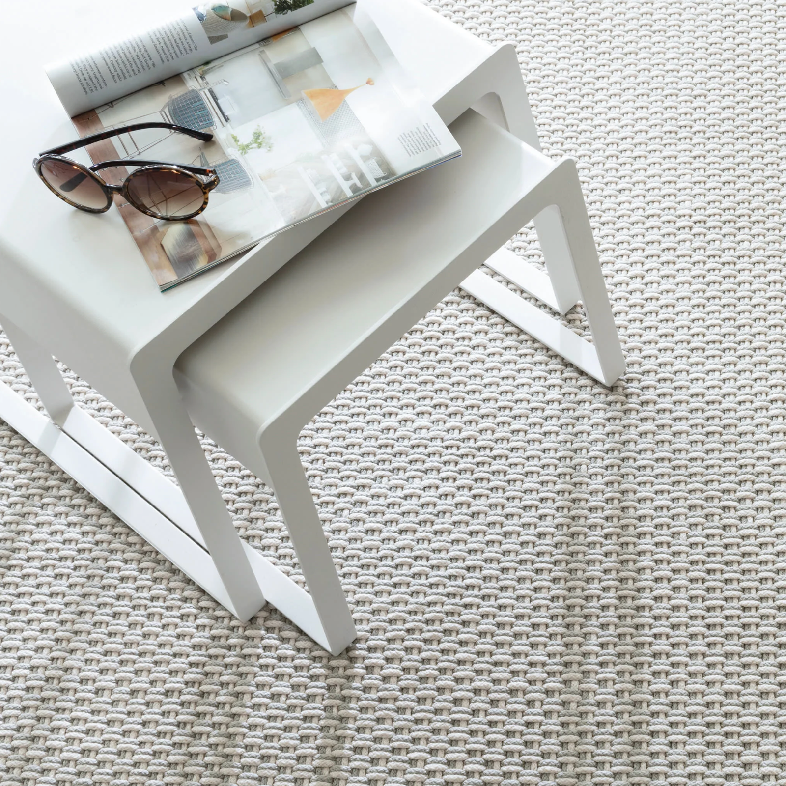 White side table with a magazine and sunglasses on a textured surface