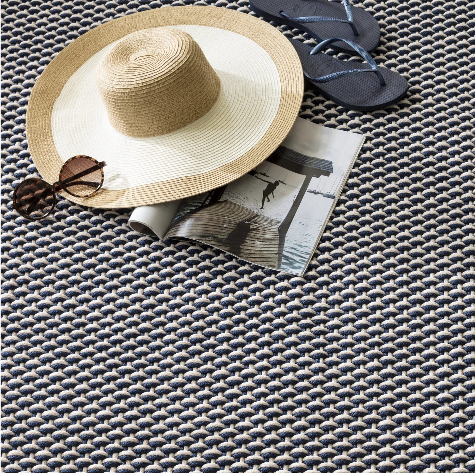 Beige straw hat, sunglasses, and magazine on a textured surface