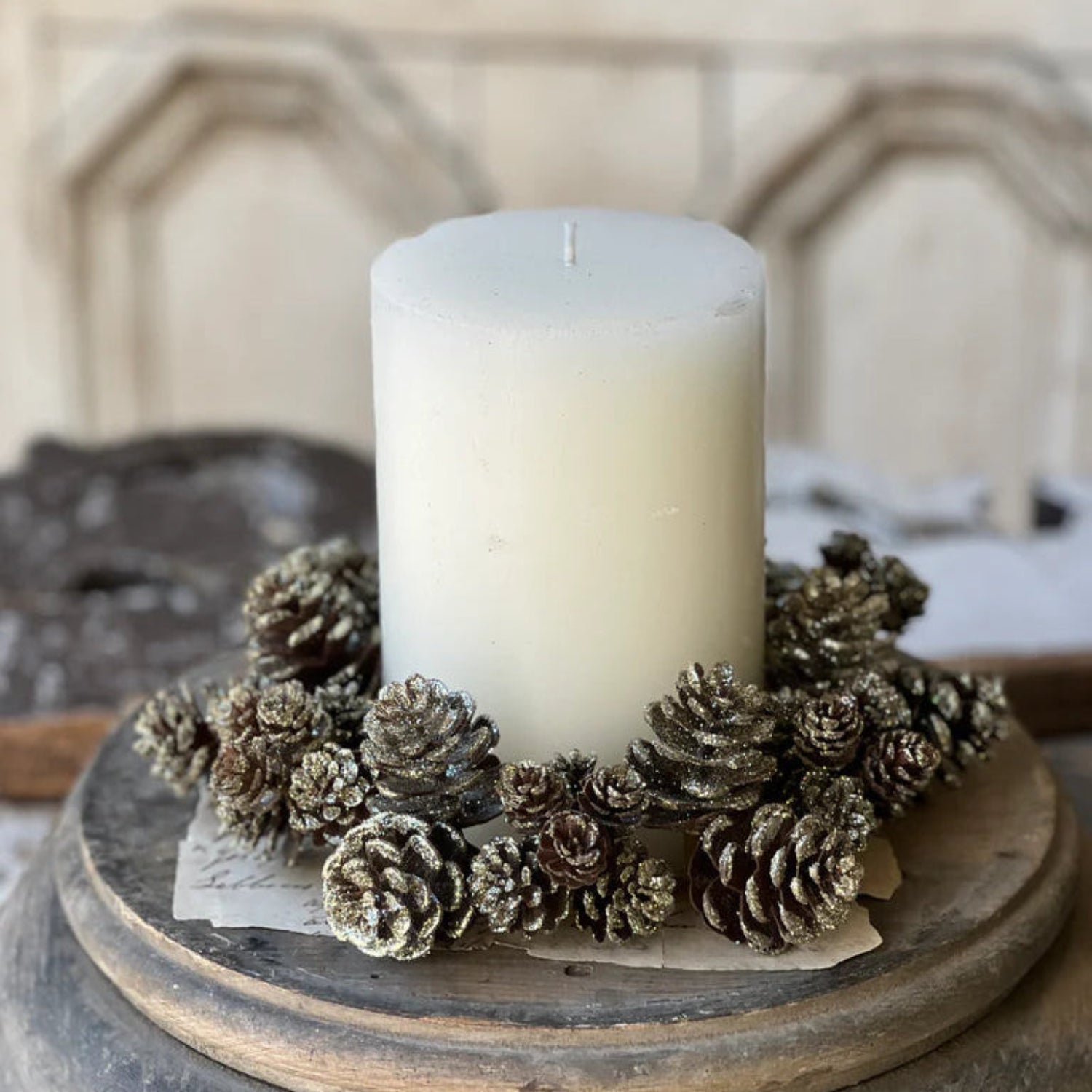 White candle on a wooden base with pinecones, set against a neutral background.