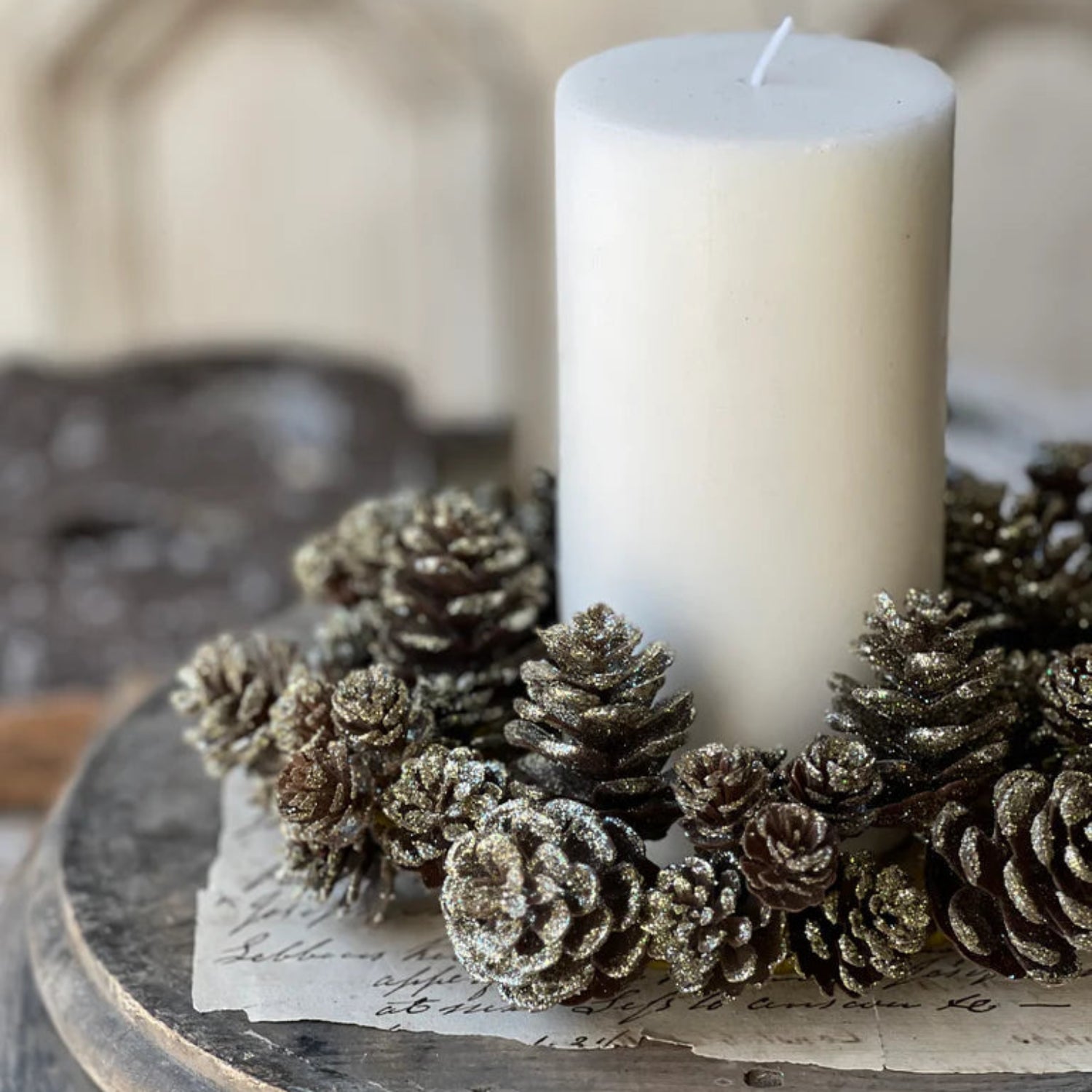 White candle surrounded by pine cones on a wooden surface with a blurred background