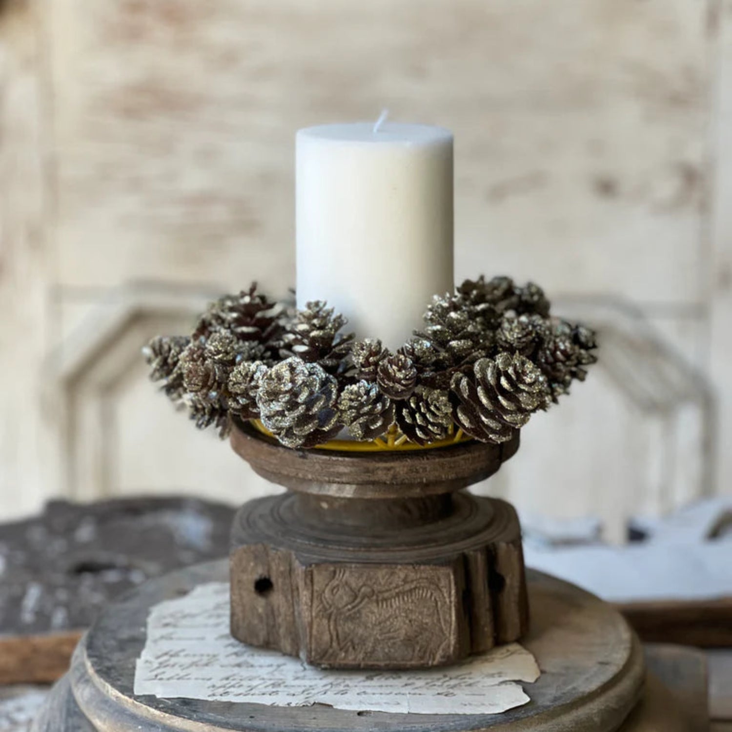 Decorative candle holder with pinecones and a candle on a wooden surface.