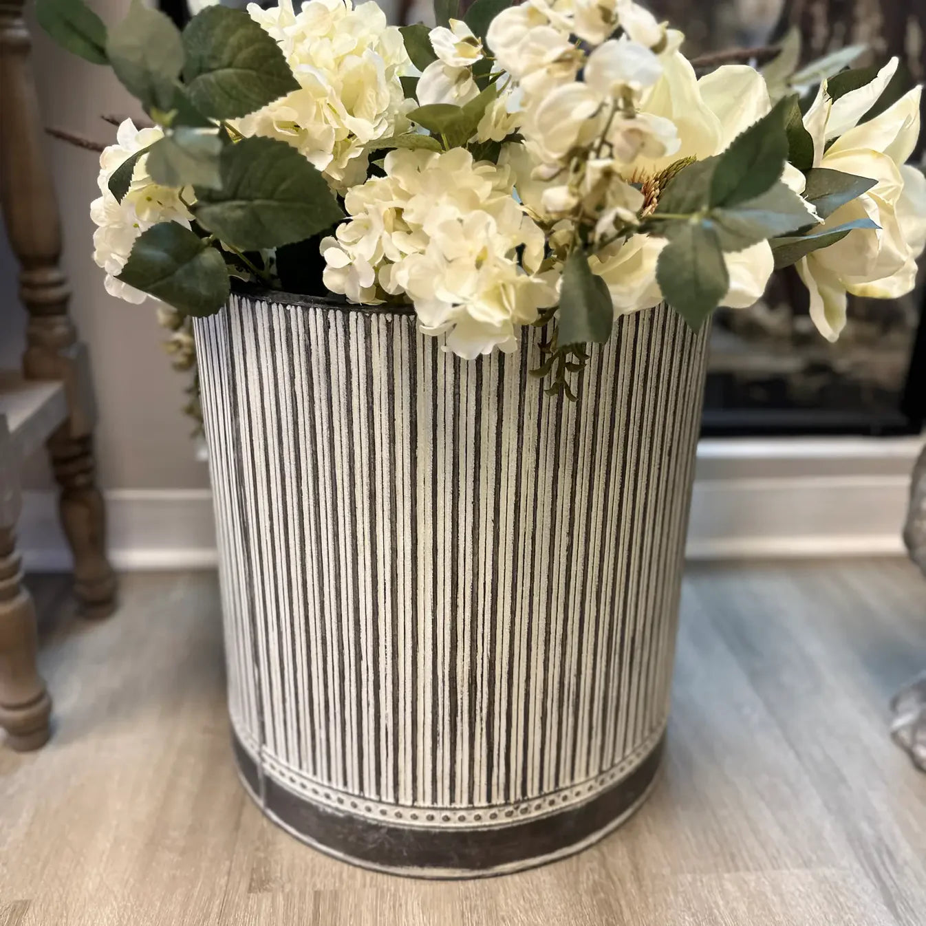 Decorative planter pot with striped pattern and white flowers on a wooden floor.