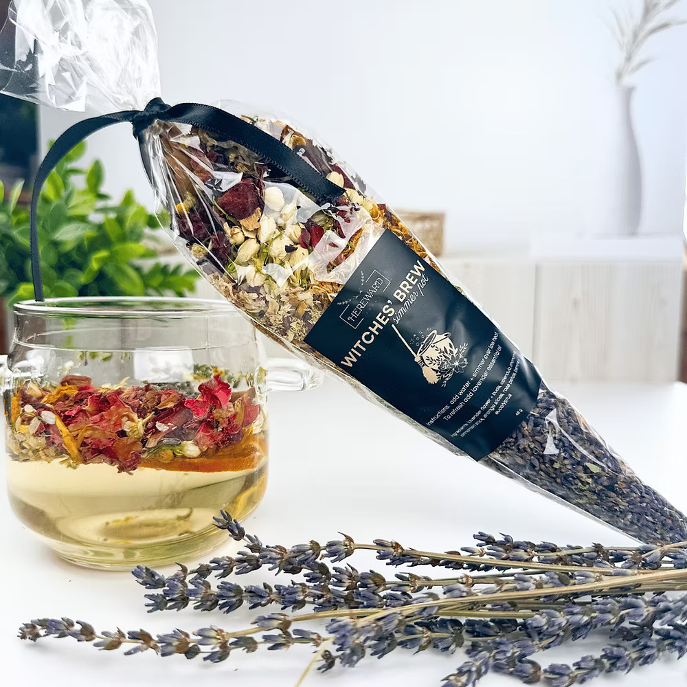 Tea package labeled 'Witches Brew' with a glass of tea and lavender on a white surface.