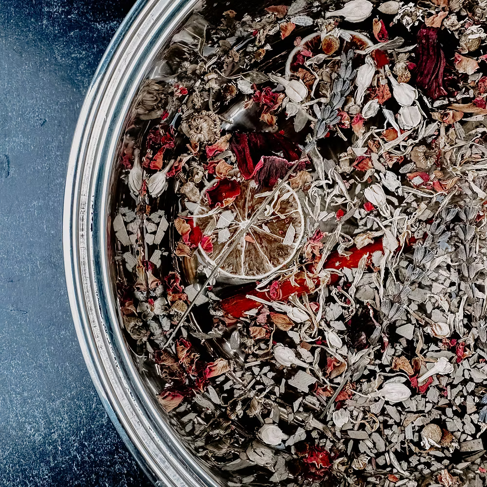 Close-up of a metal container filled with dried herbs and flowers on a blue surface.