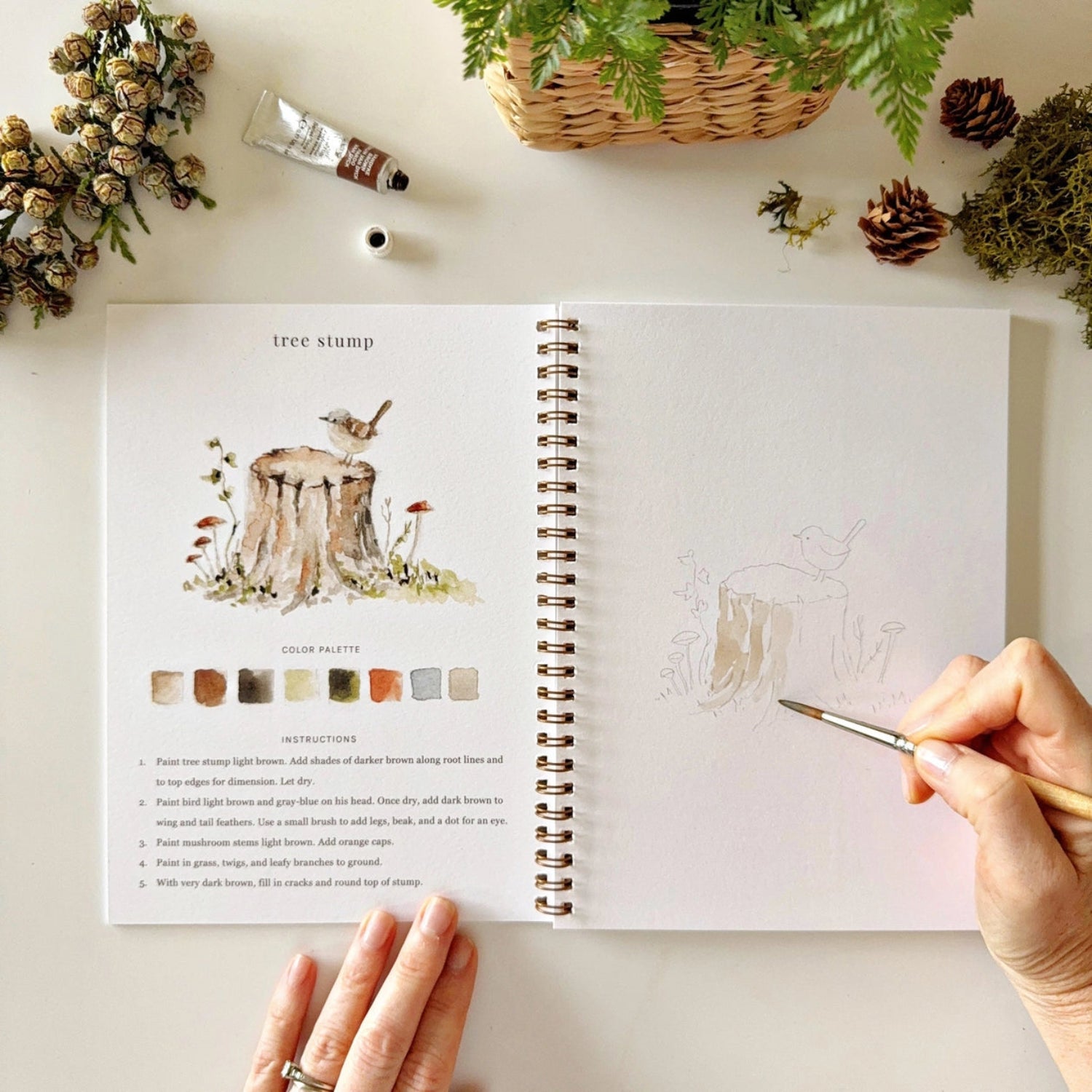 Artistic coloring book with a tree stump illustration and color palette, held by a person with a pen.