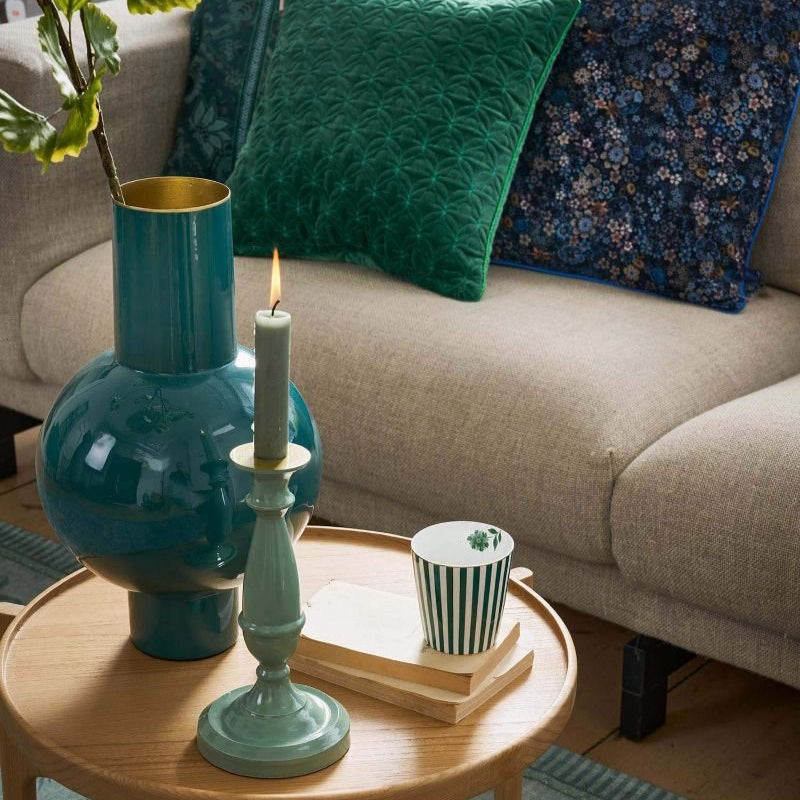 Teal vase and candle on a wooden side table with a beige sofa and decorative pillows in the background.