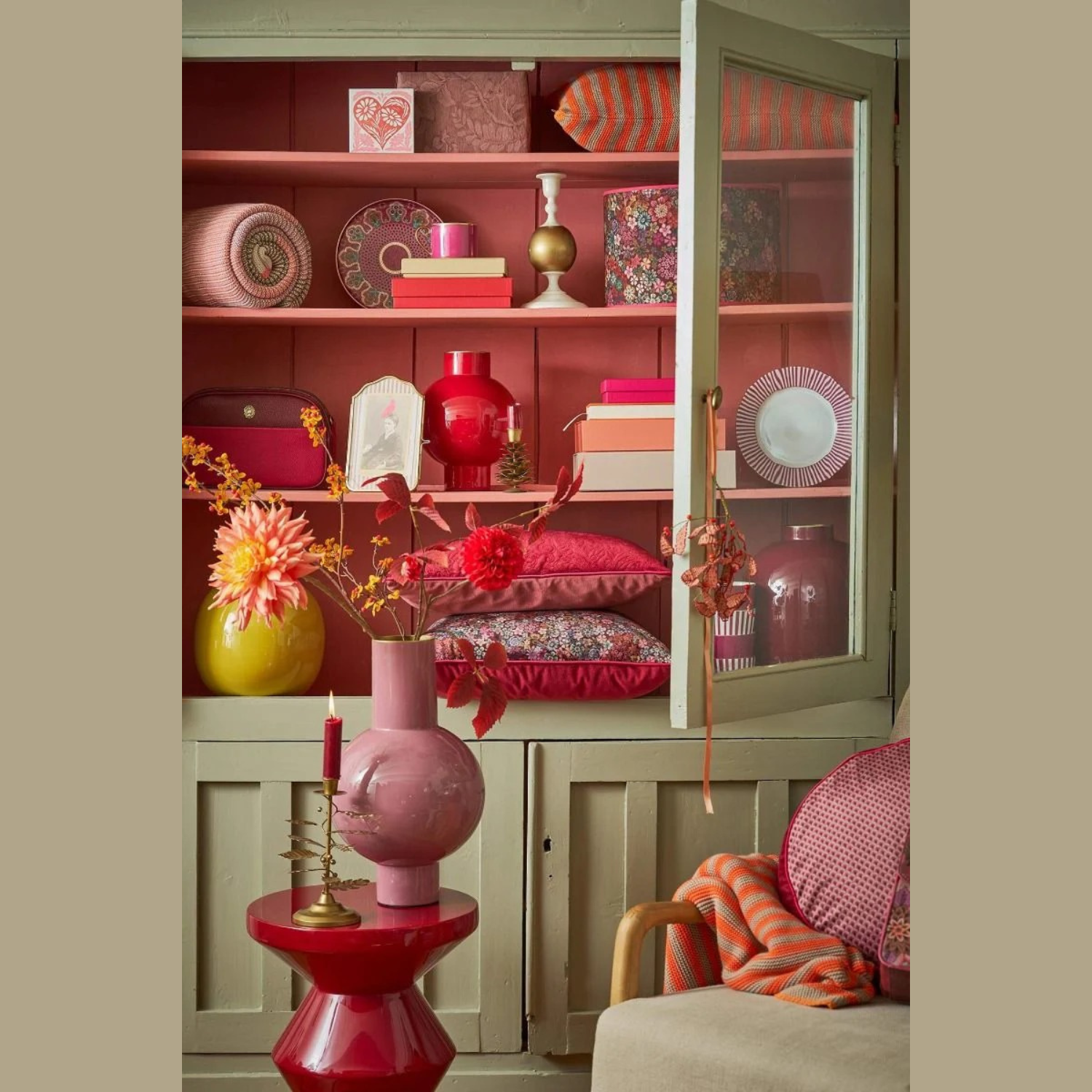 Decorative interior with a green cabinet, pink and red vases, and floral arrangements.