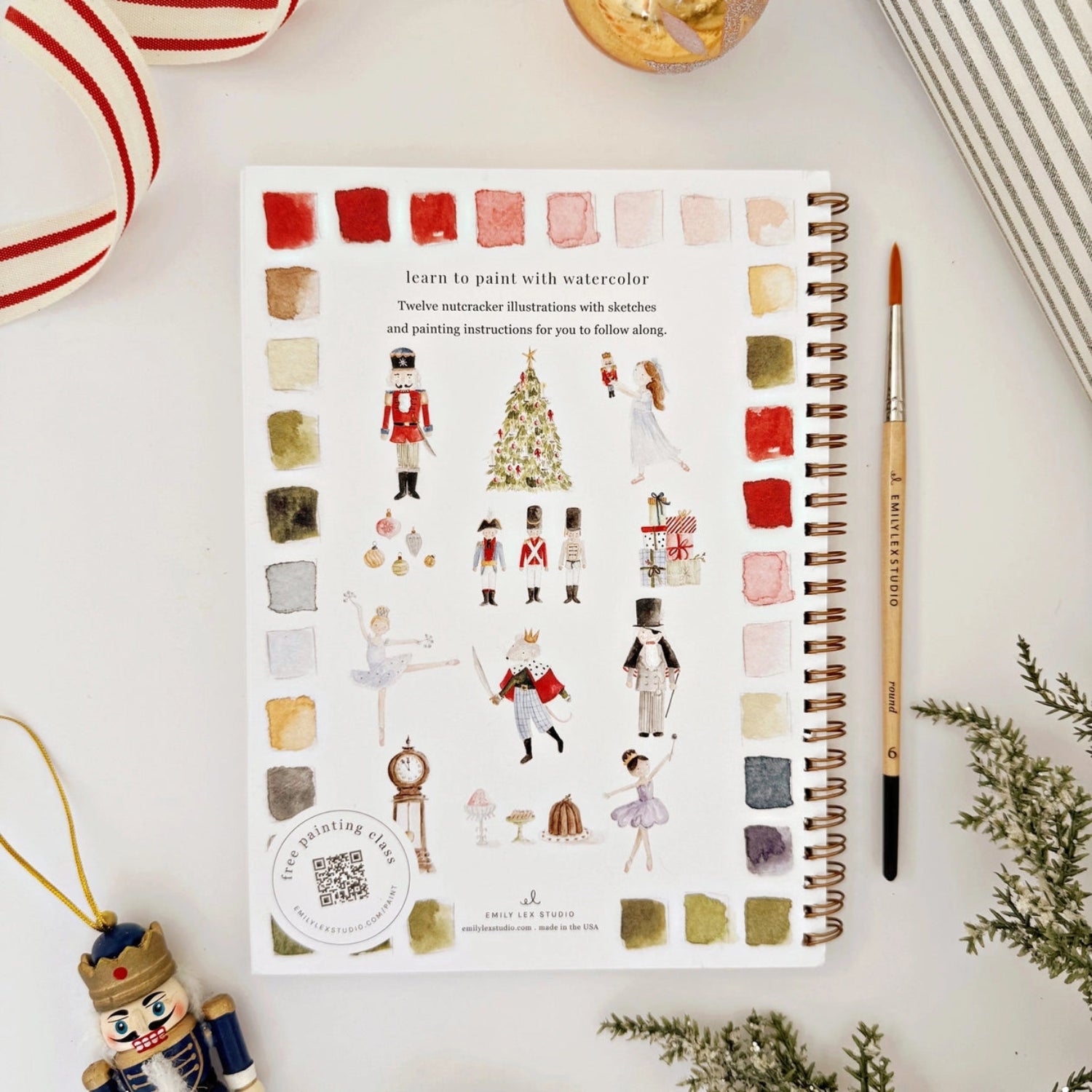 Notebook with watercolor illustrations and color swatches on a white surface with decorative items.