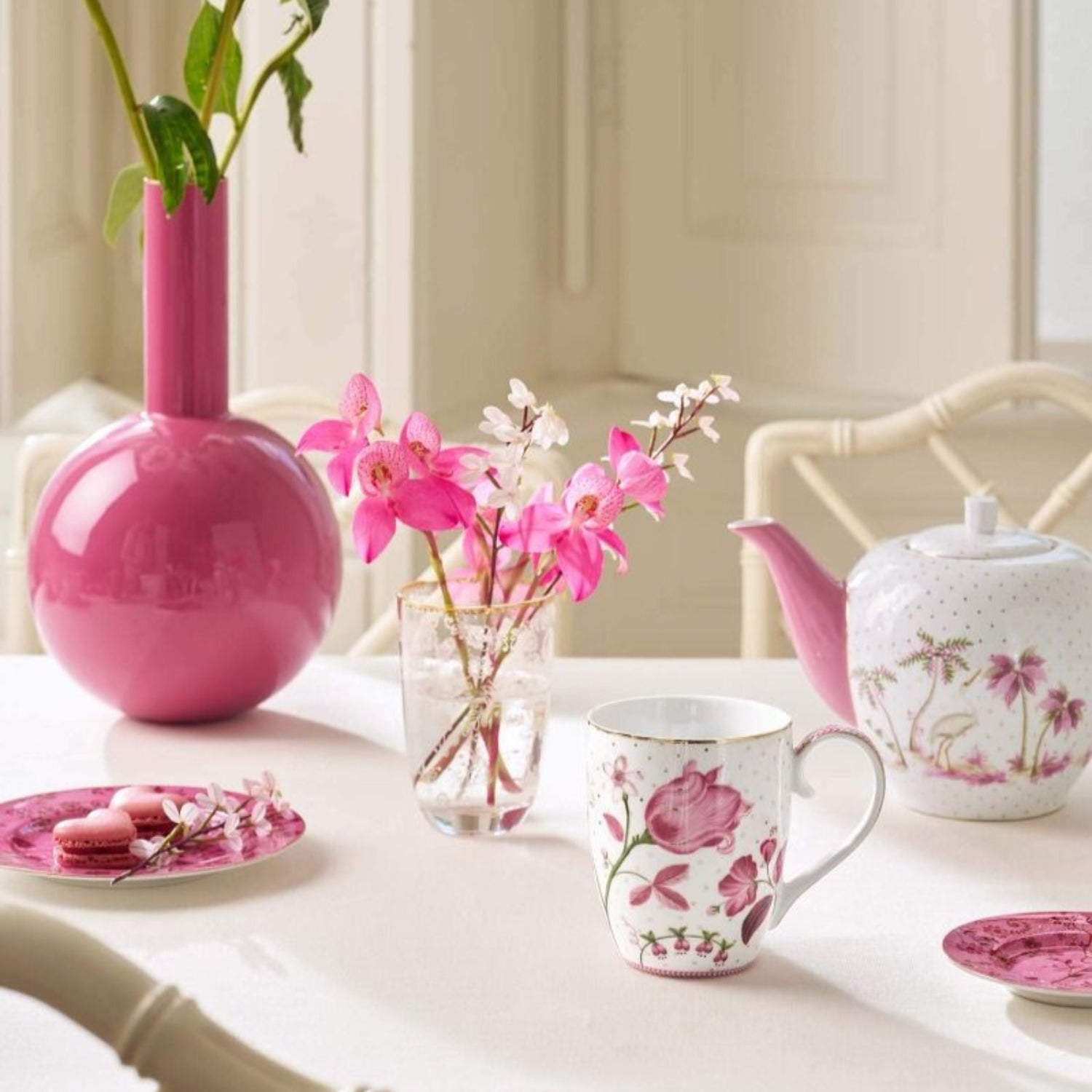 Tea set with floral design on a table with pink and white flowers.