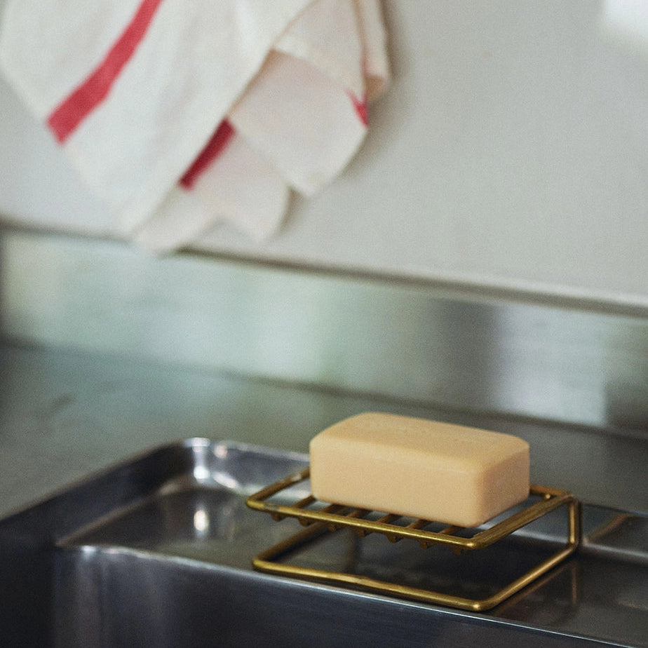 Bar of soap on a gold soap dish over a sink with a towel in the background