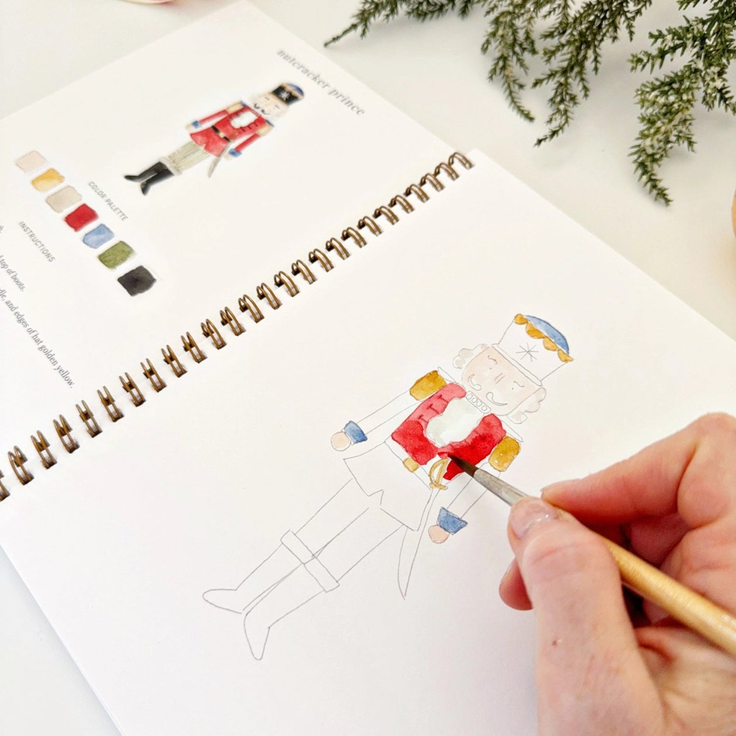 Person coloring a Christmas-themed illustration in a notebook with a color swatch.