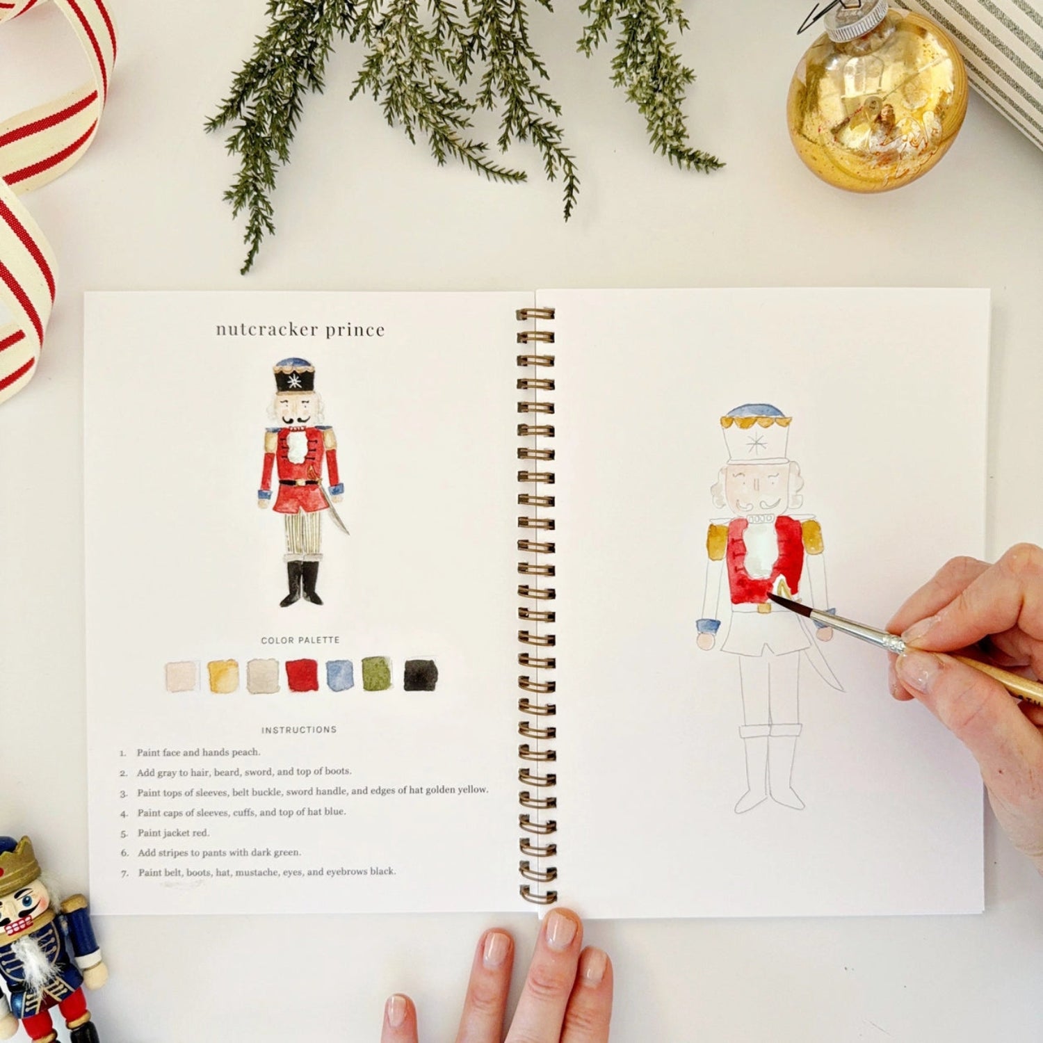 Open book with a nutcracker illustration and color palette, surrounded by Christmas decorations.