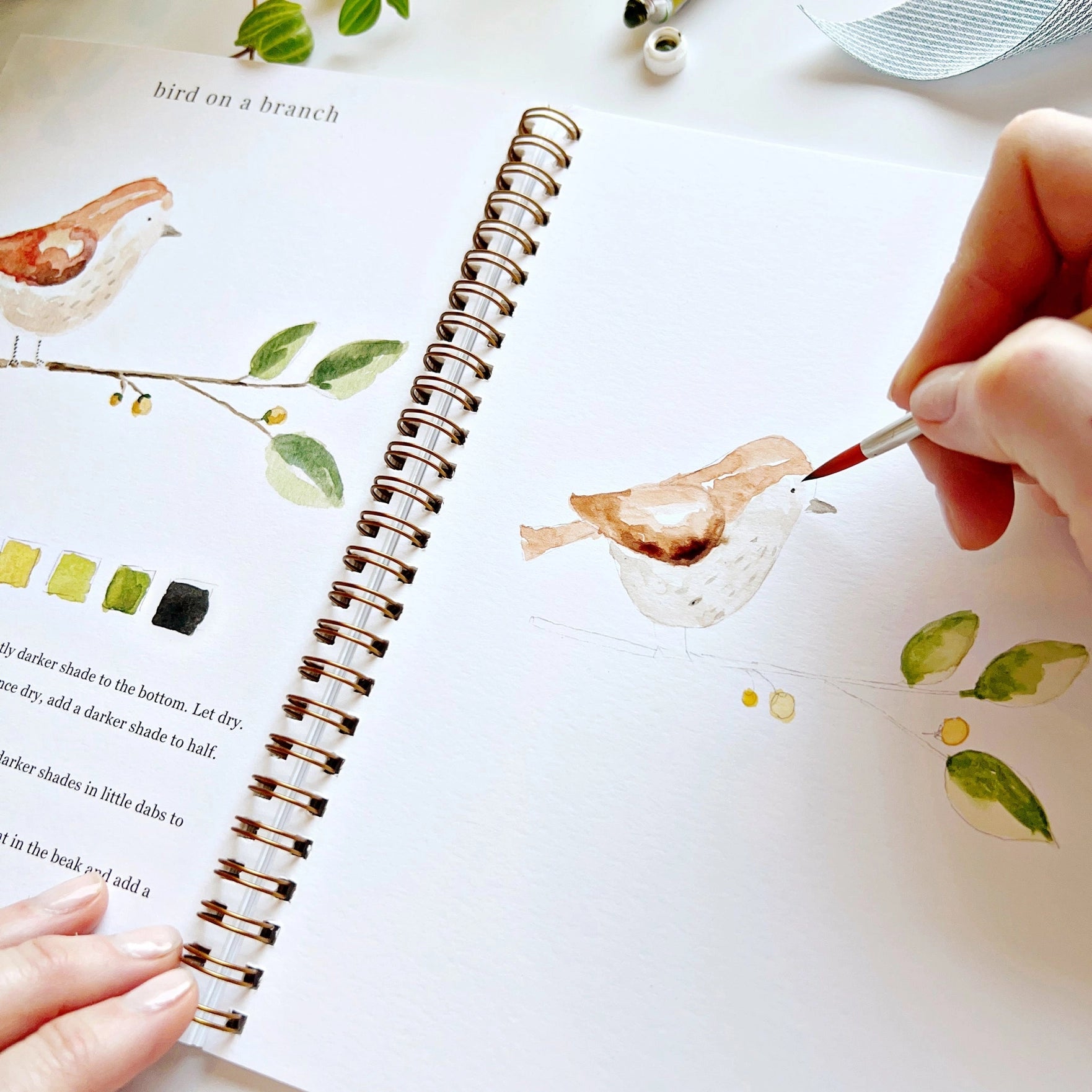 Person painting a bird illustration in a notebook with a paintbrush