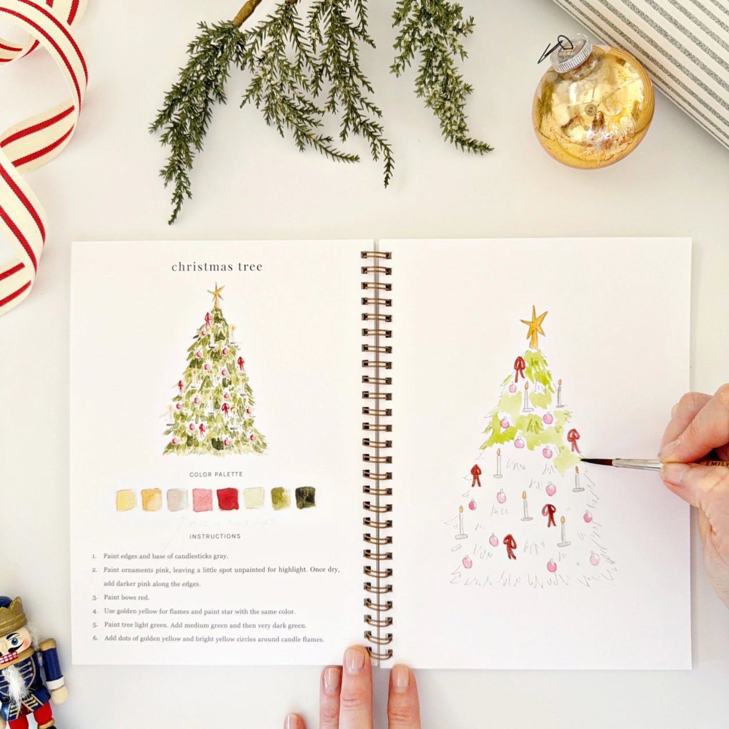 Open book with Christmas tree illustrations and a hand holding a pen.