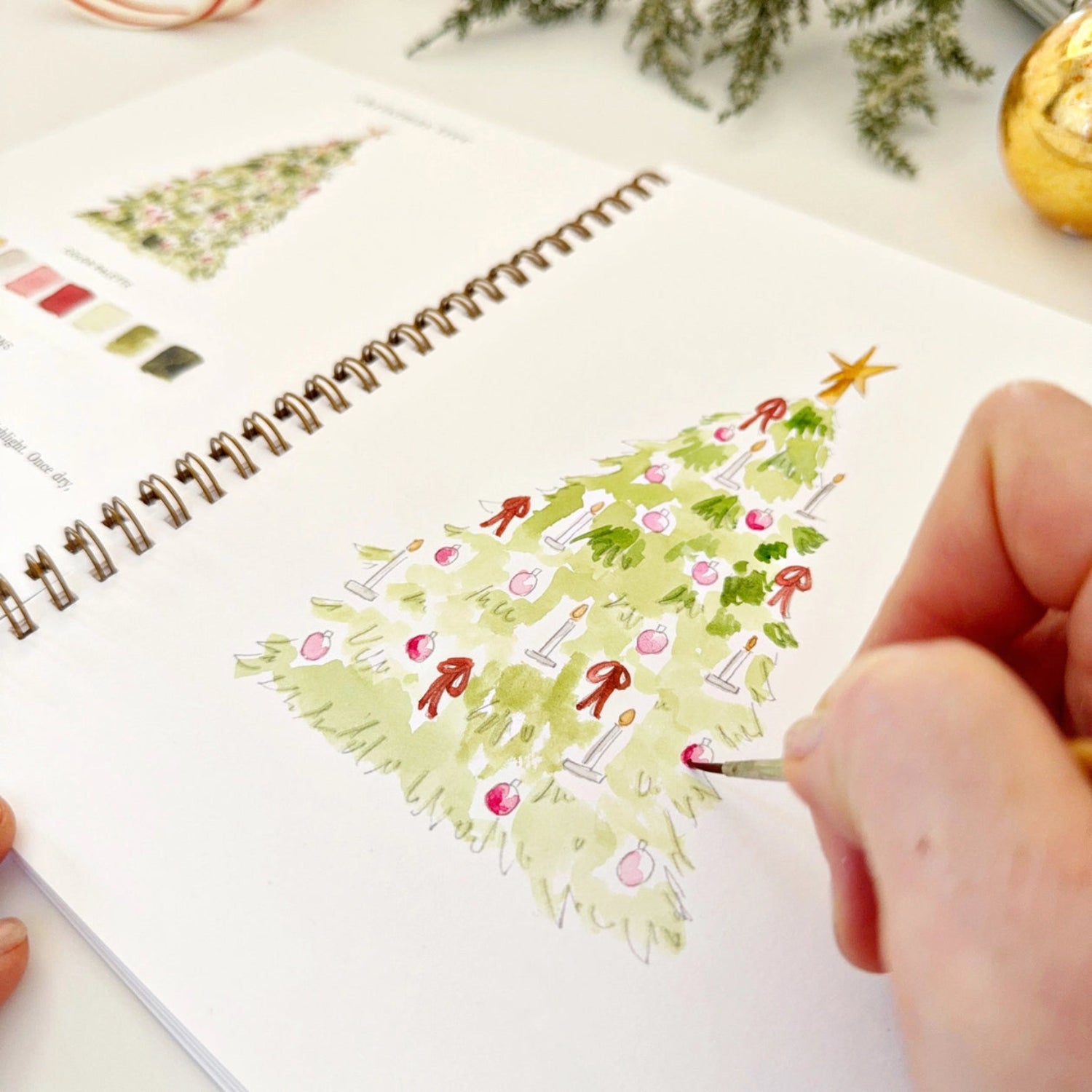Person drawing a Christmas tree on a notebook with a pen.