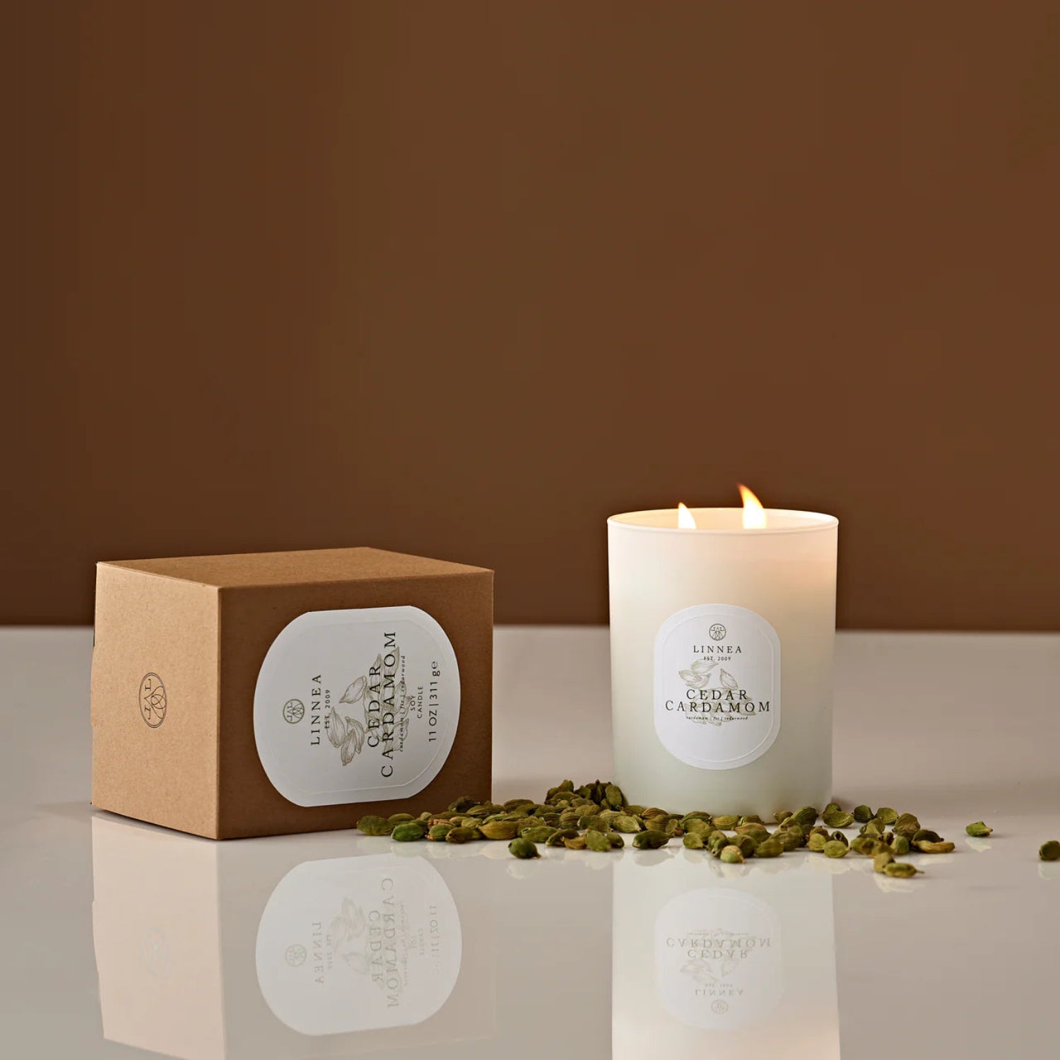 Candle with a label and a box on a reflective surface with a brown background