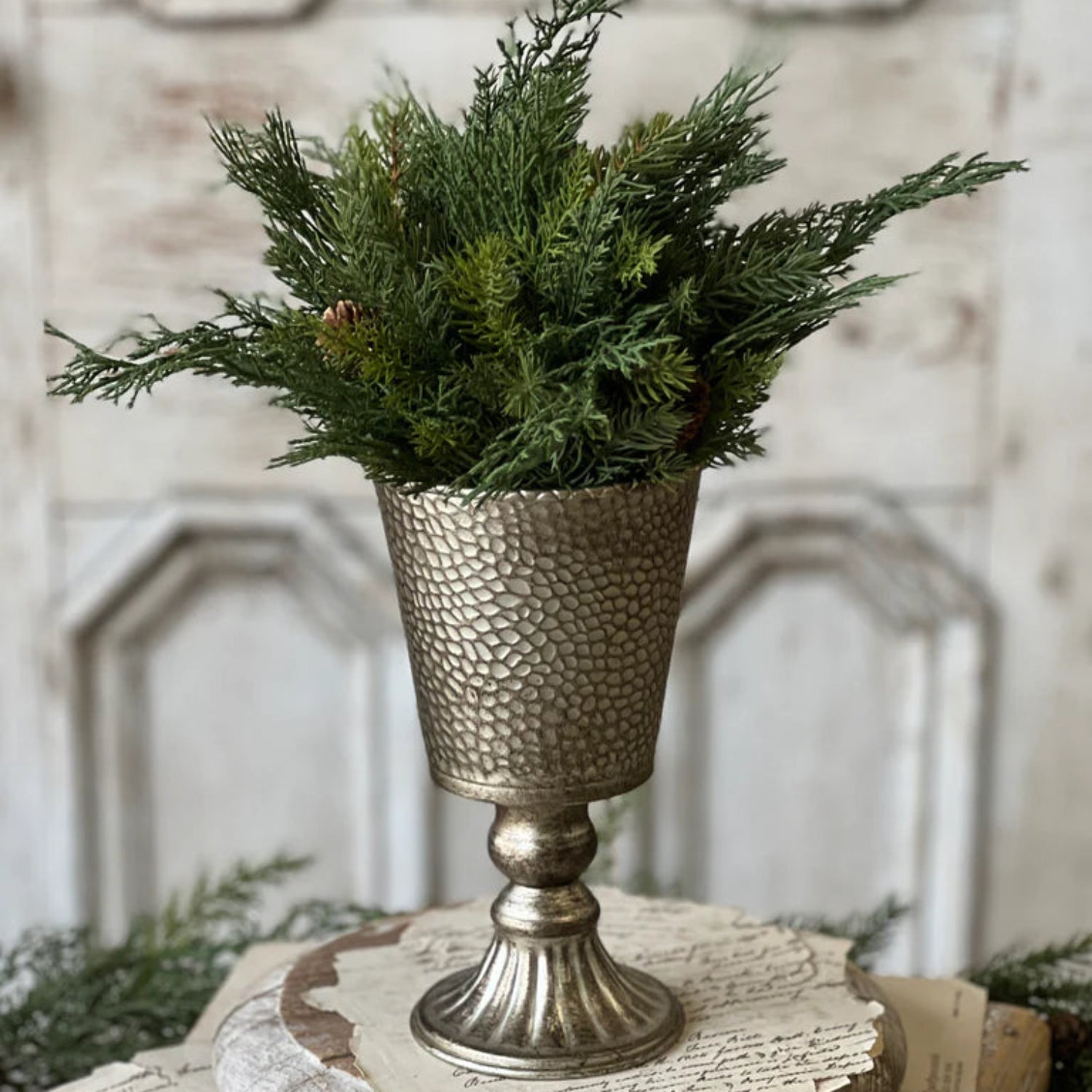 Decorative arrangement with a metallic vase and greenery on a textured surface.