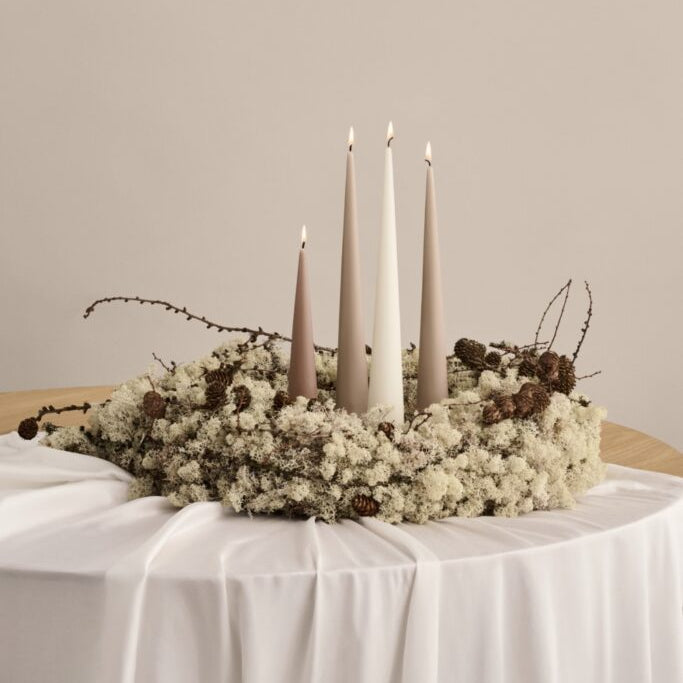 Decorative centerpiece with candles and flowers on a table against a plain background