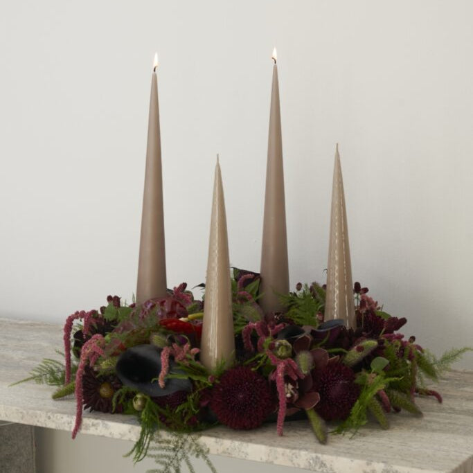 Decorative arrangement with candles and flowers on a marble surface against a white wall.