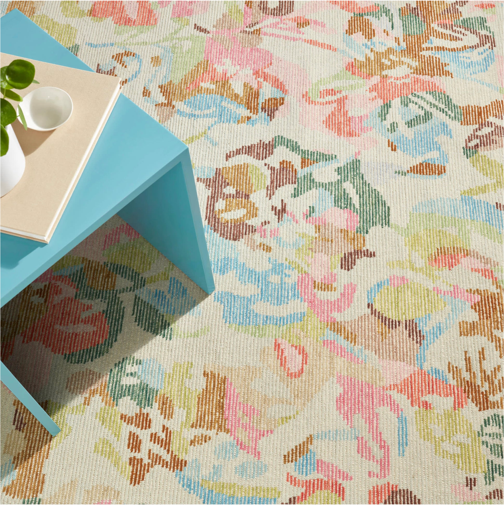 Floral patterned rug with a blue table and white cup on top
