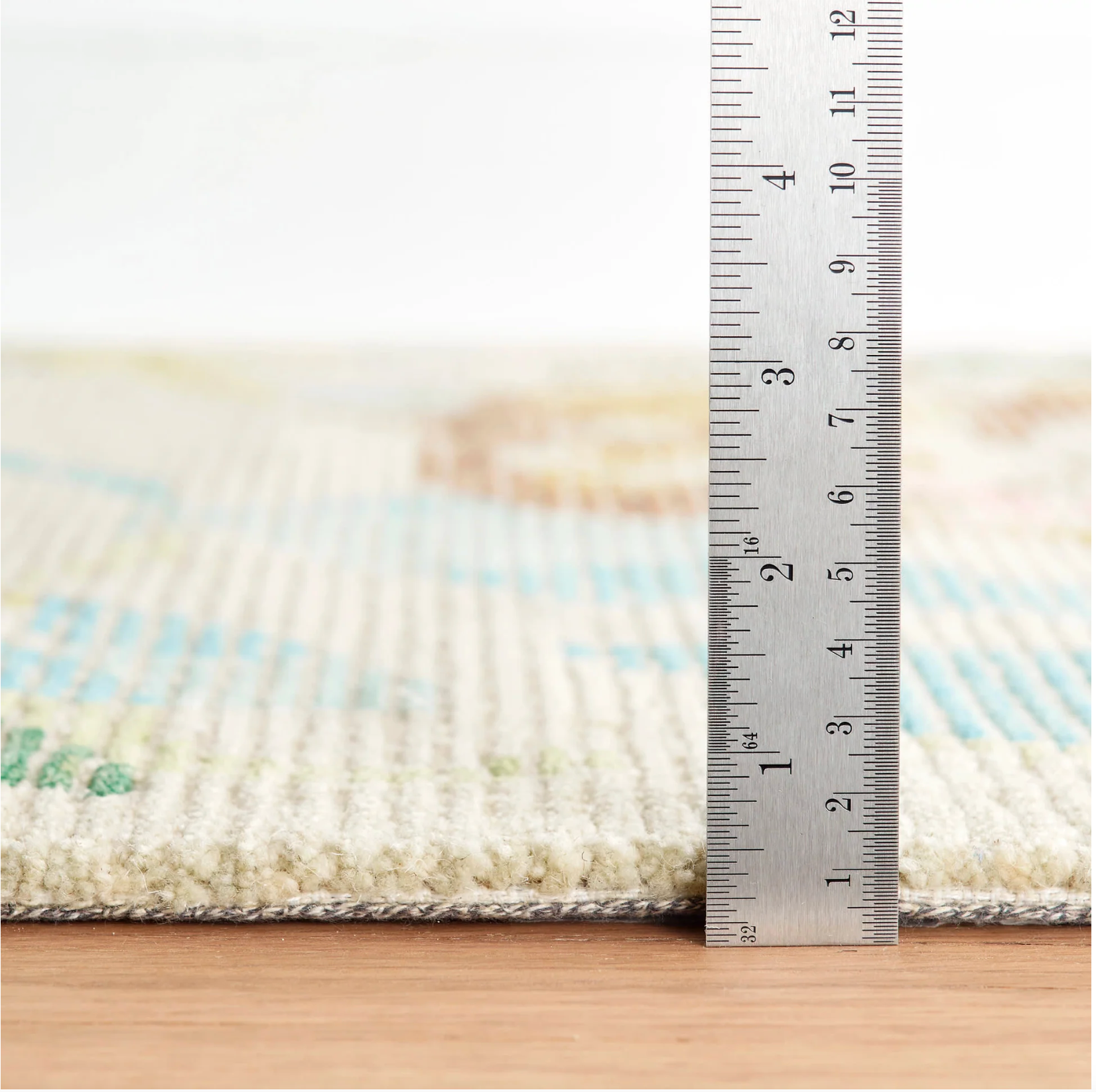 Rug with a ruler showing its thickness on a wooden floor.