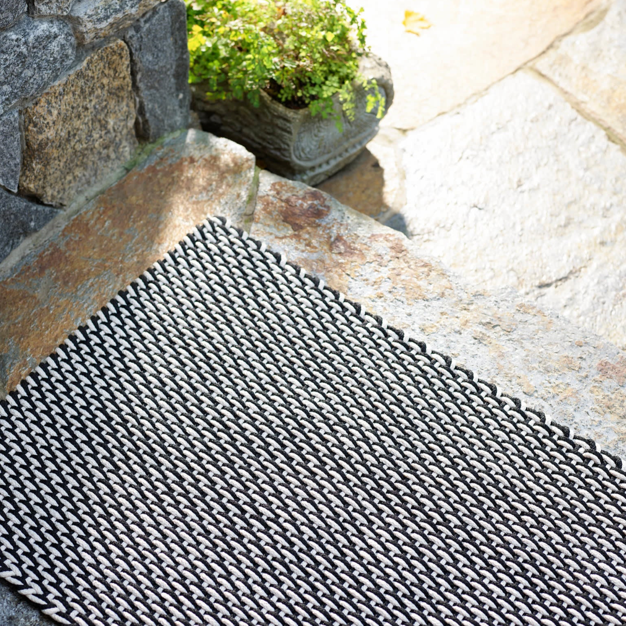 Black and white textured mat on a stone floor with a plant in the background
